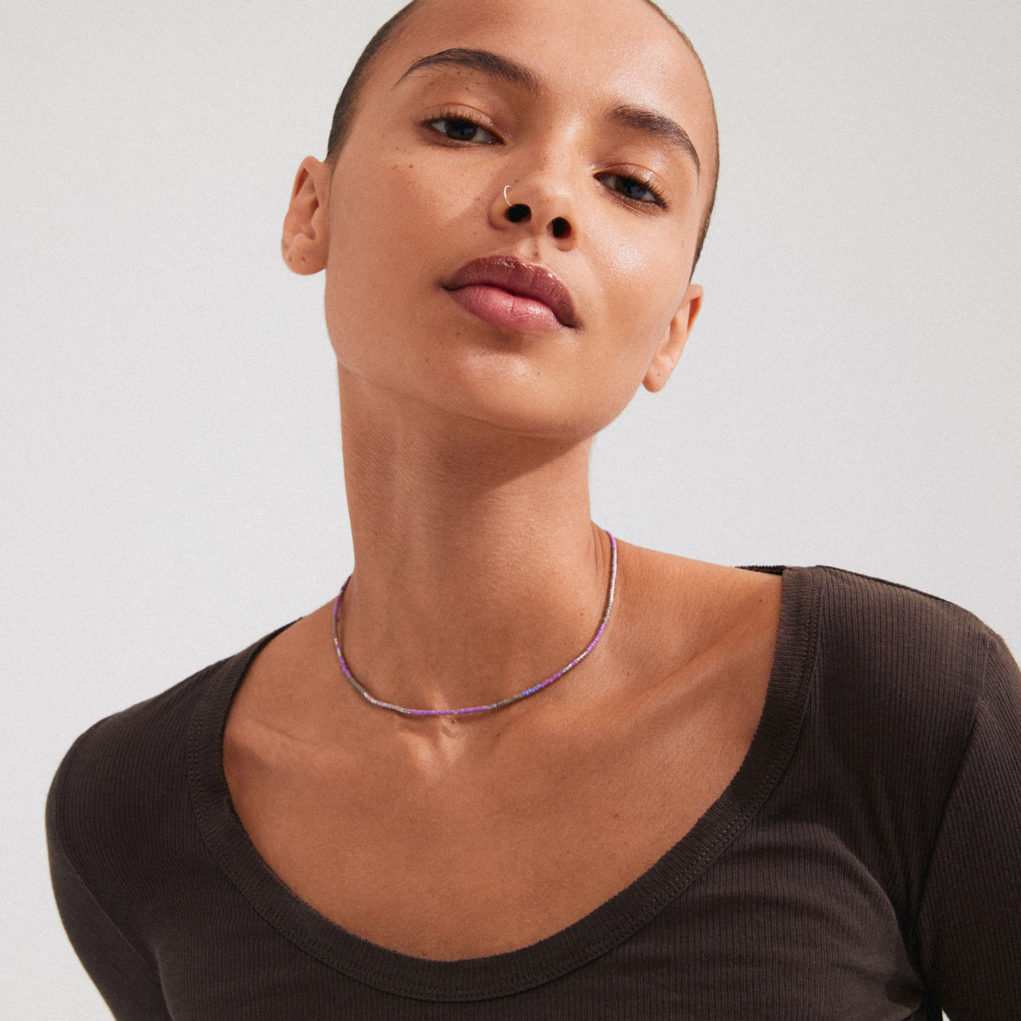 Woman wearing Pilgrim's ALISON necklace, featuring purple glass beads and a silver-plated chain, styled close to the neck for a layered look.