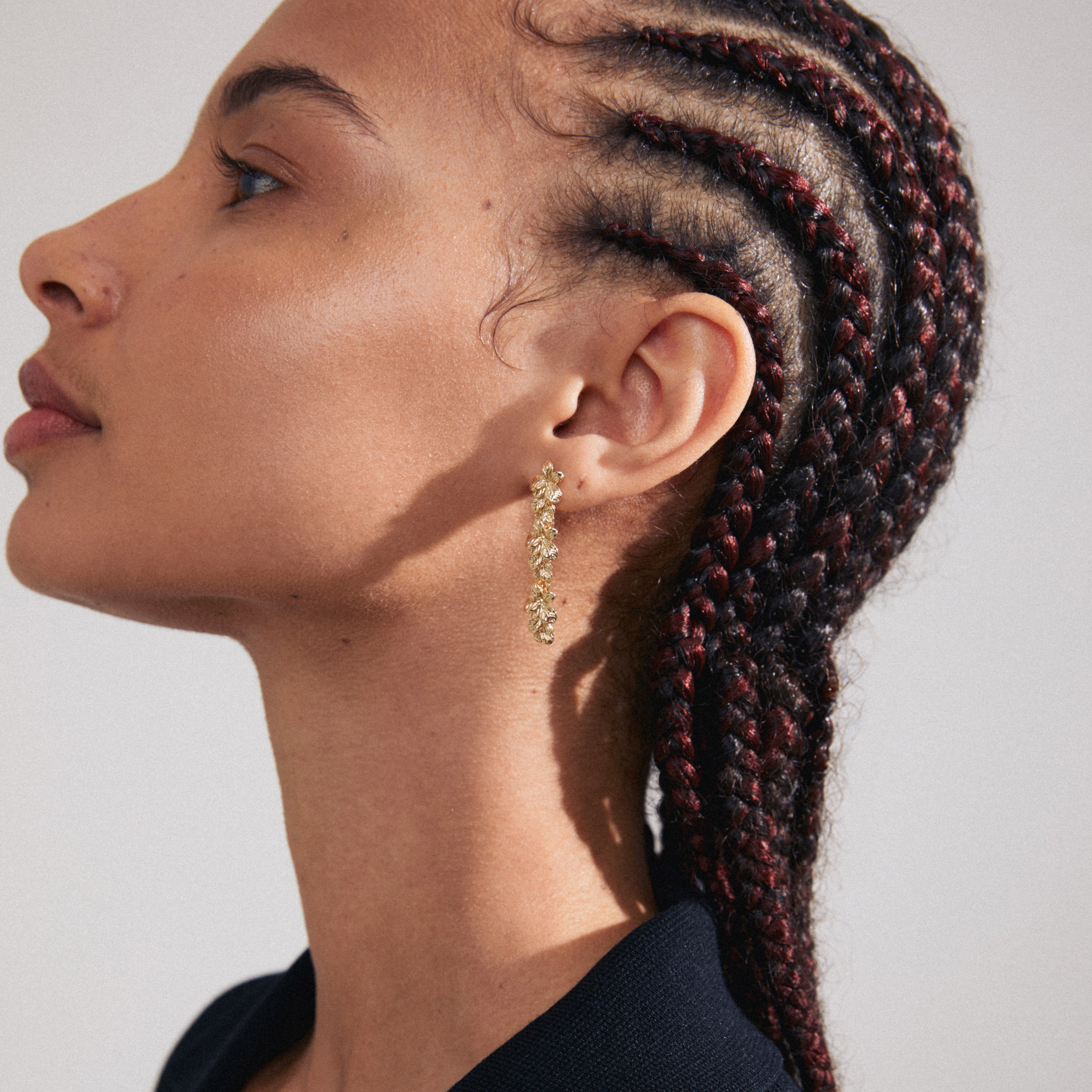 Close-up of a woman wearing the CHARMAINE gold-plated earrings with a braided hairstyle, showcasing the earrings' intricate, nature-inspired design from Pilgrim.