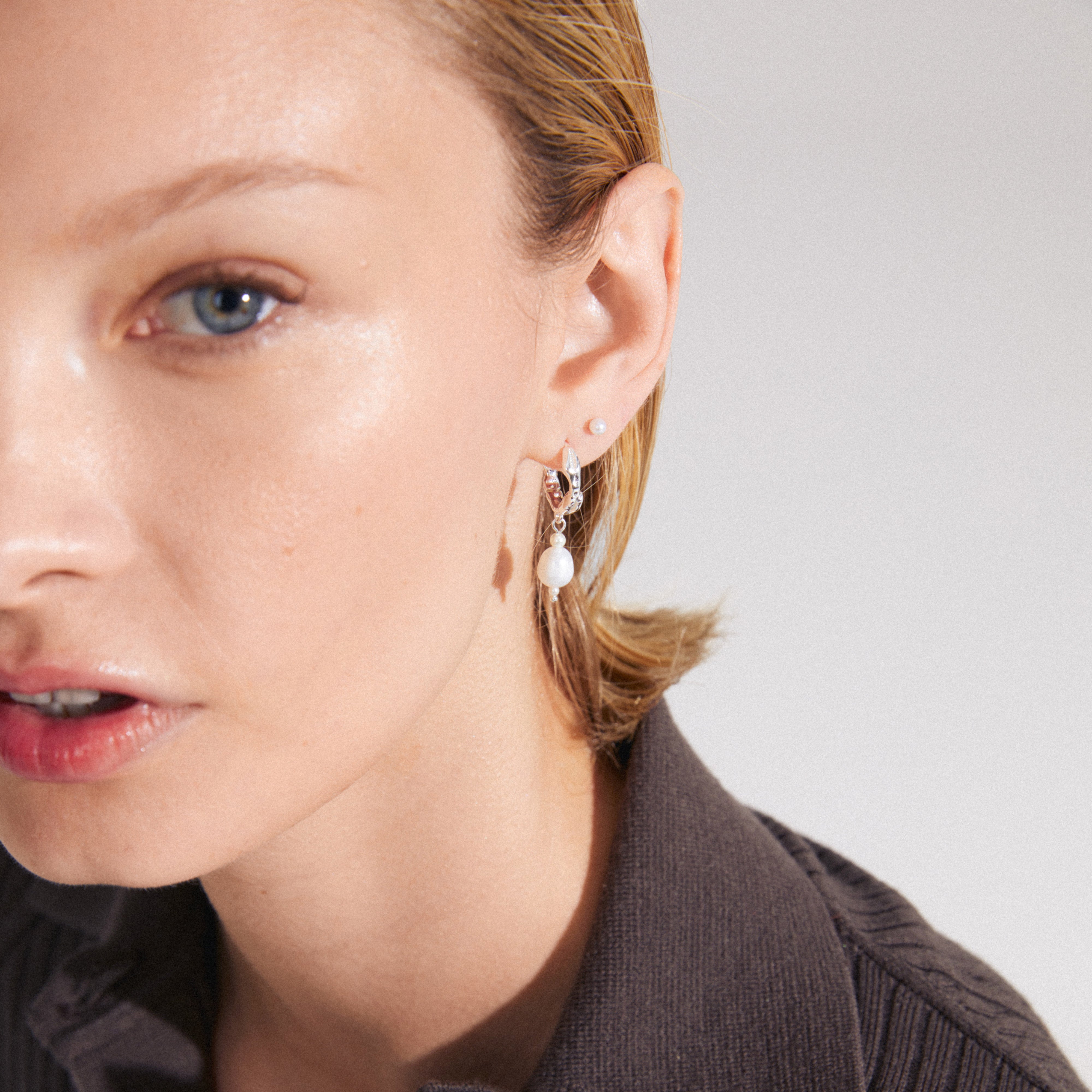 Young woman wearing Pilgrim's CONSTANCE earrings 2-in-1 set: silver-plated hoops with teardrop freshwater pearl pendants and small glasspearl studs, highlighting timeless elegance.