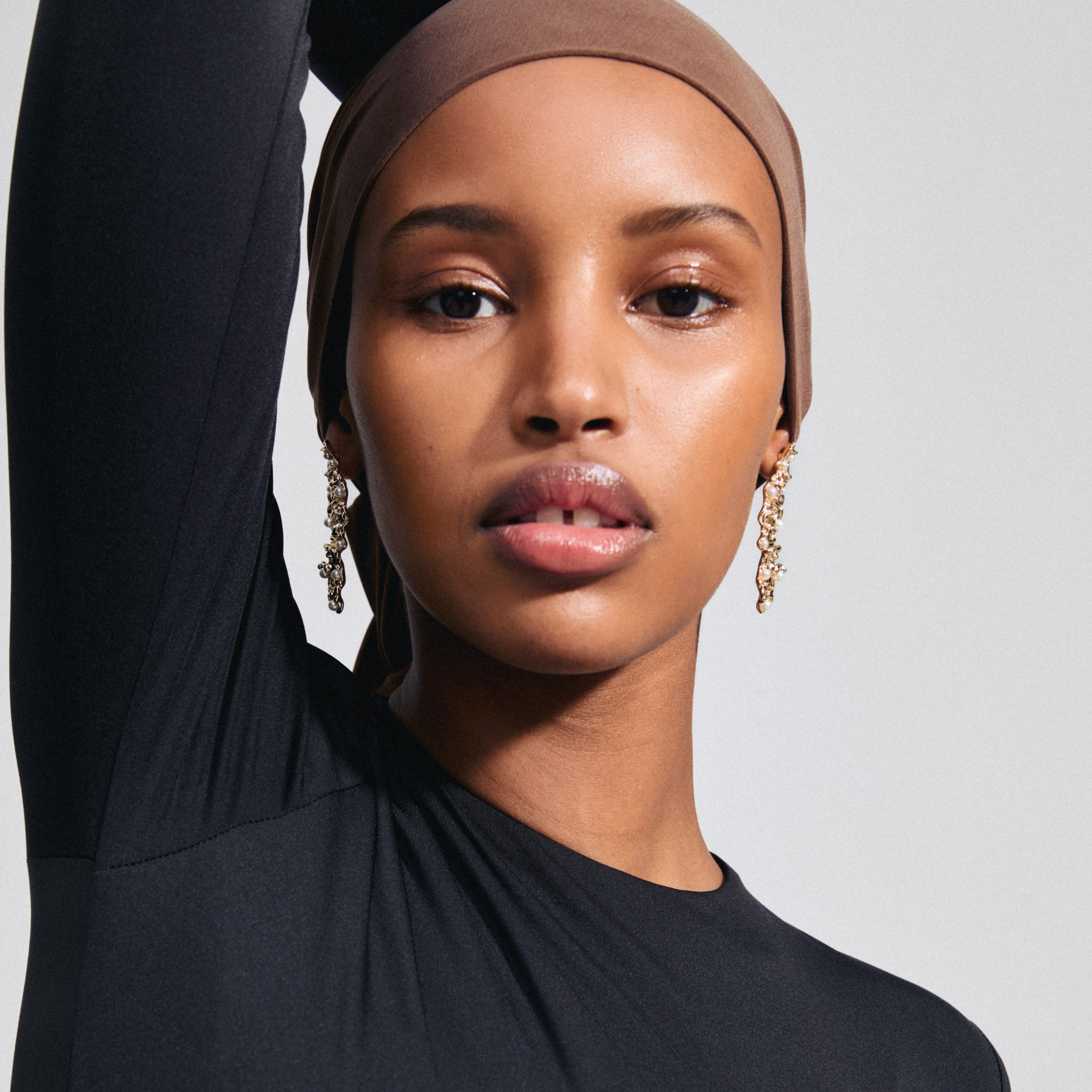 A woman wearing JUDE gold-plated earrings by Pilgrim, featuring an organic design with pearlescent beads, embodying a unique and adventurous style.