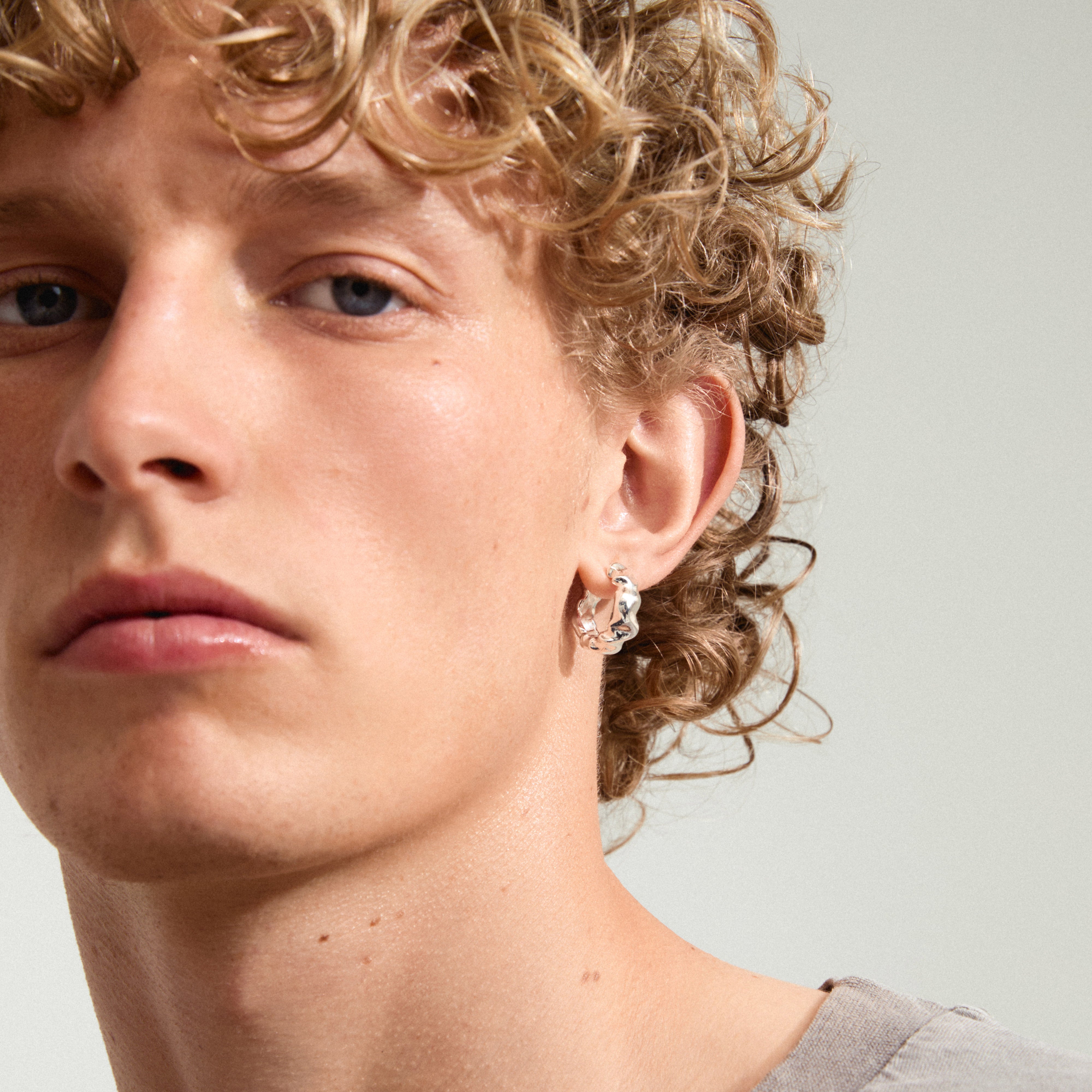 Close-up of a young person wearing the ELLIOT earrings silver-plated by Pilgrim, featuring a unique wavy design and made from recycled materials.