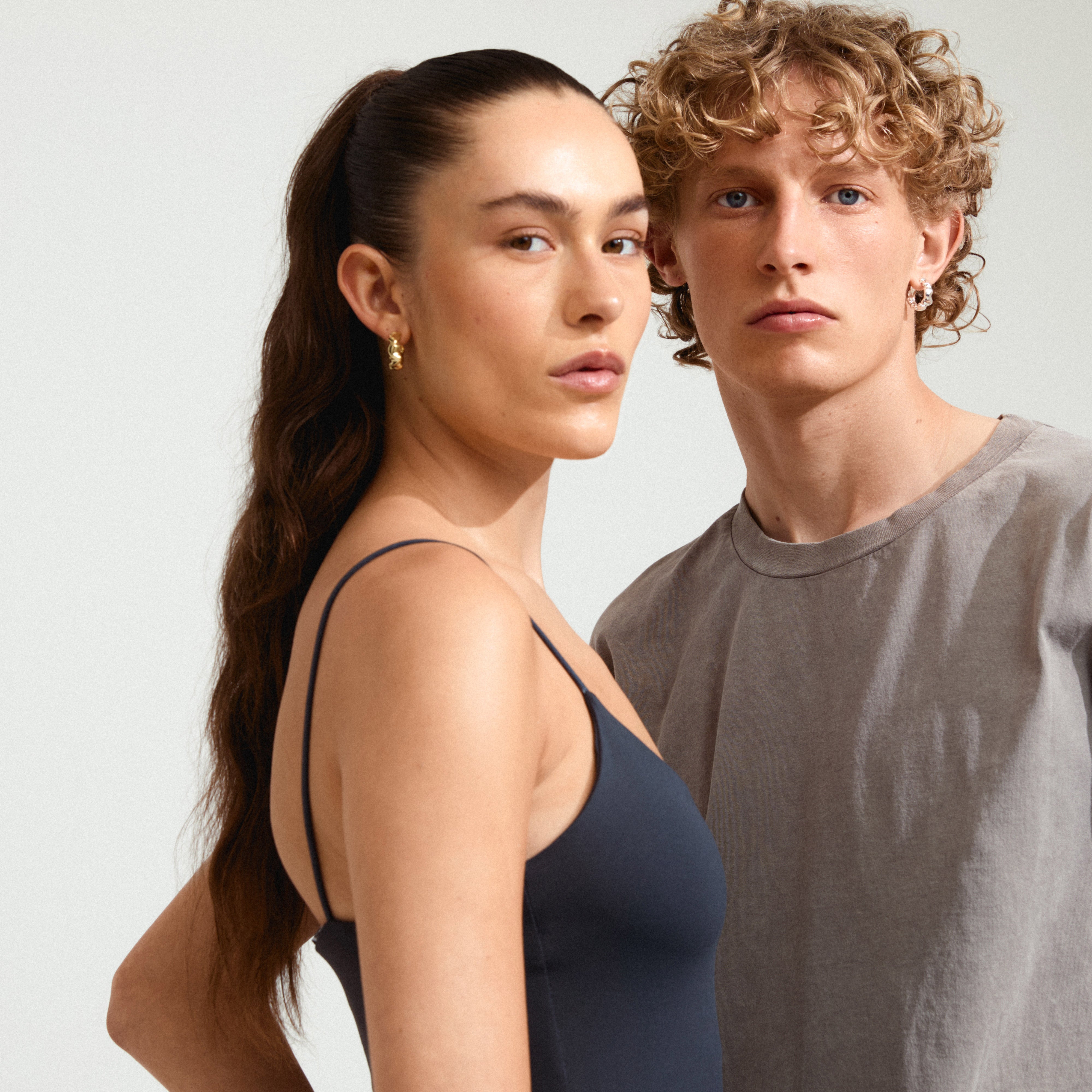 Two young adults wearing ELLIOT silver-plated hoop earrings from Pilgrim, showcasing the earrings' elegant, wavy design and eco-friendly craftsmanship.
