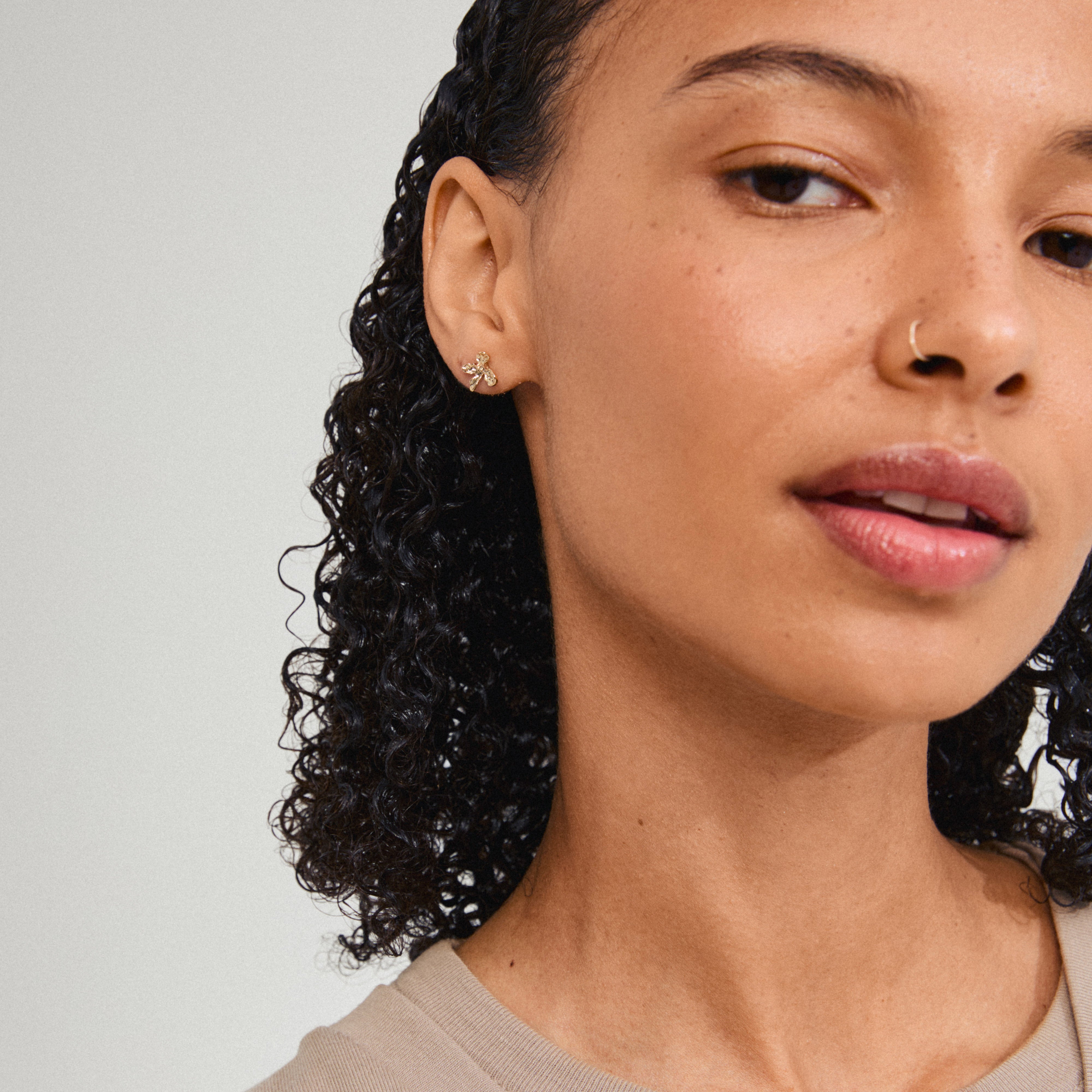 AGLAIA earrings gold-plated on woman with curly hair and nose ring, showcasing delicate flower design inspired by nature, embodying Pilgrim's summer elegance.
