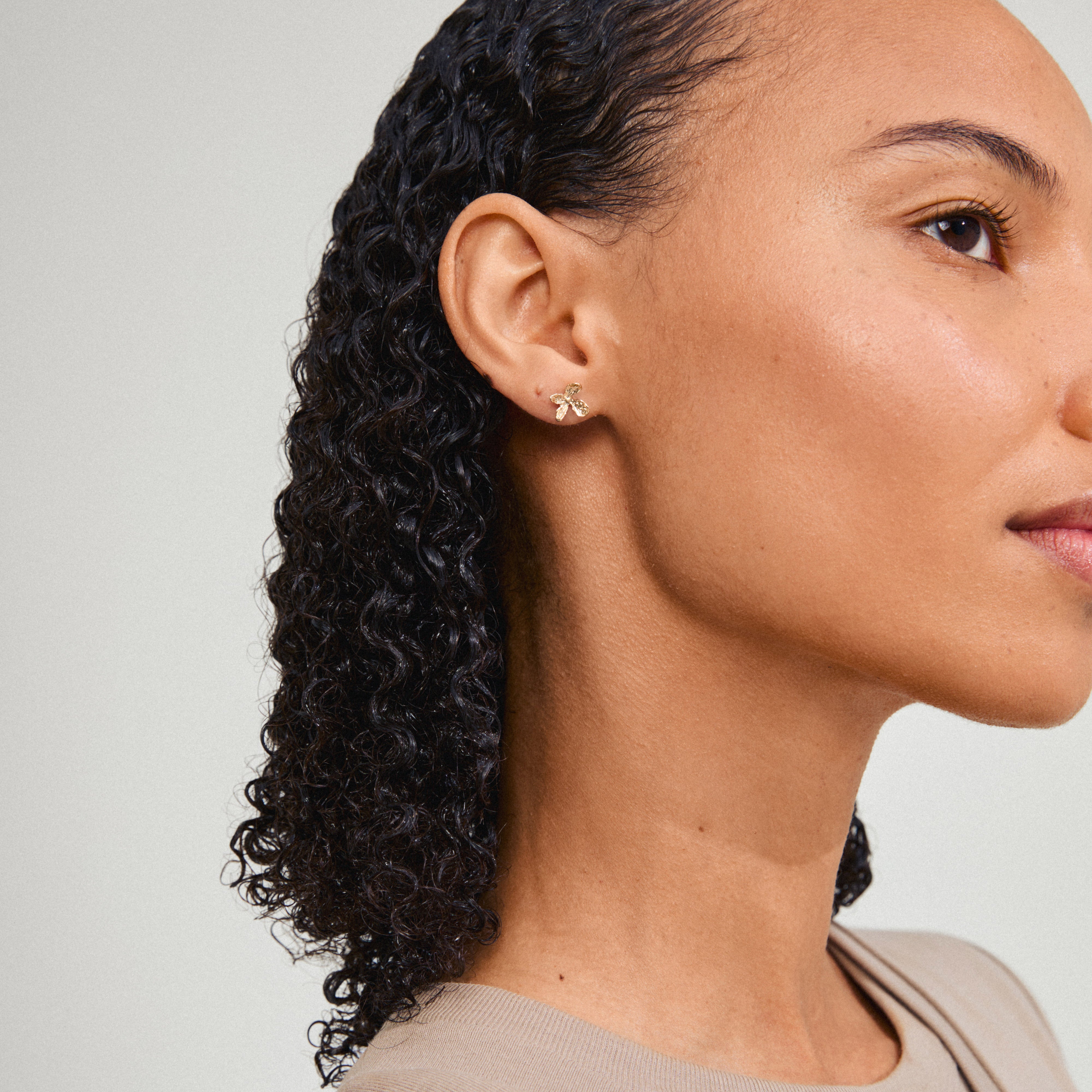 AGLAIA gold-plated stud earrings with a delicate flower design, visible on a woman's ear, embody Pilgrim's nature-inspired elegance and sustainable craftsmanship.