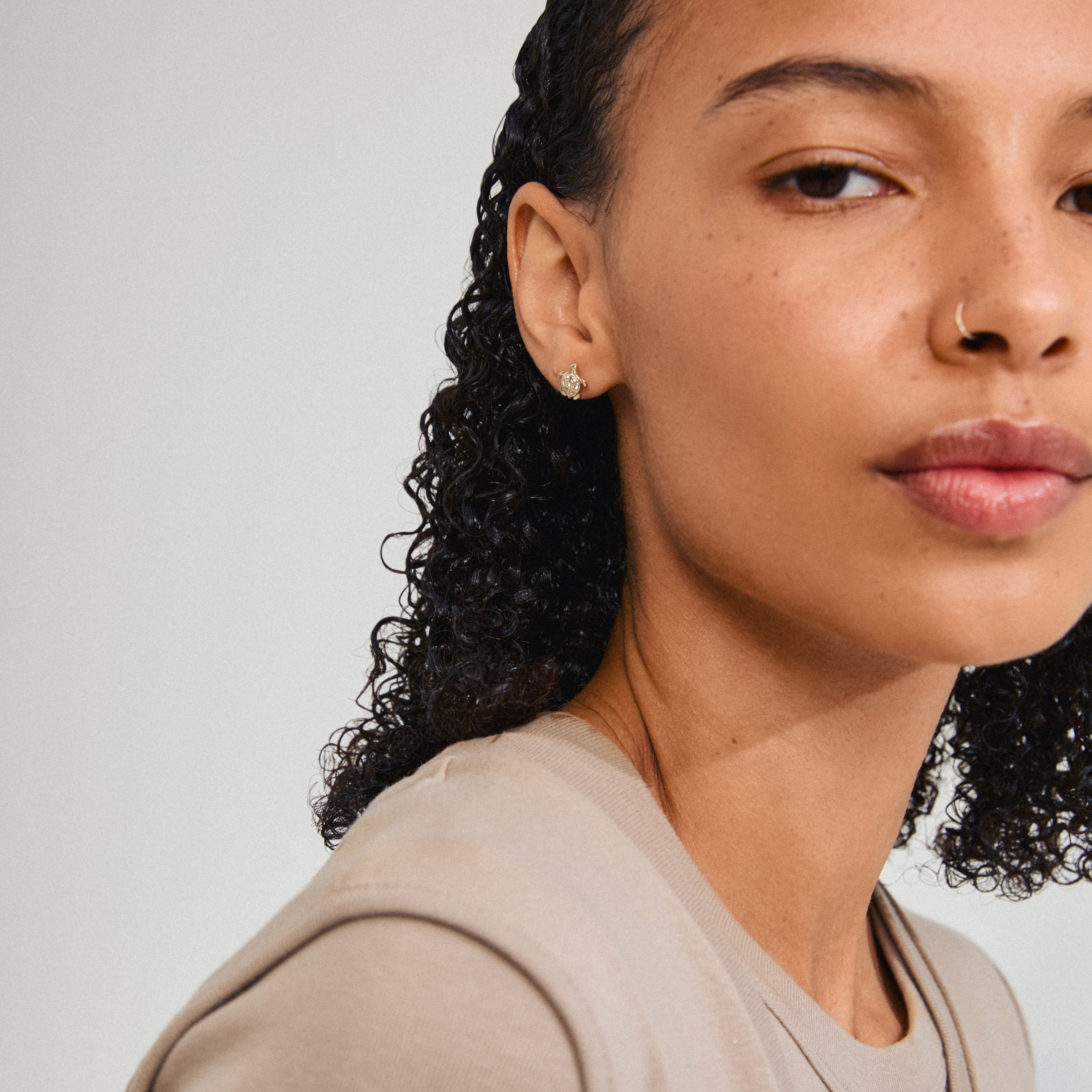 Close-up of a woman wearing Pilgrim's gold-plated ARCHER earrings with sparkling crystals and turtle design, embodying nature-inspired elegance.