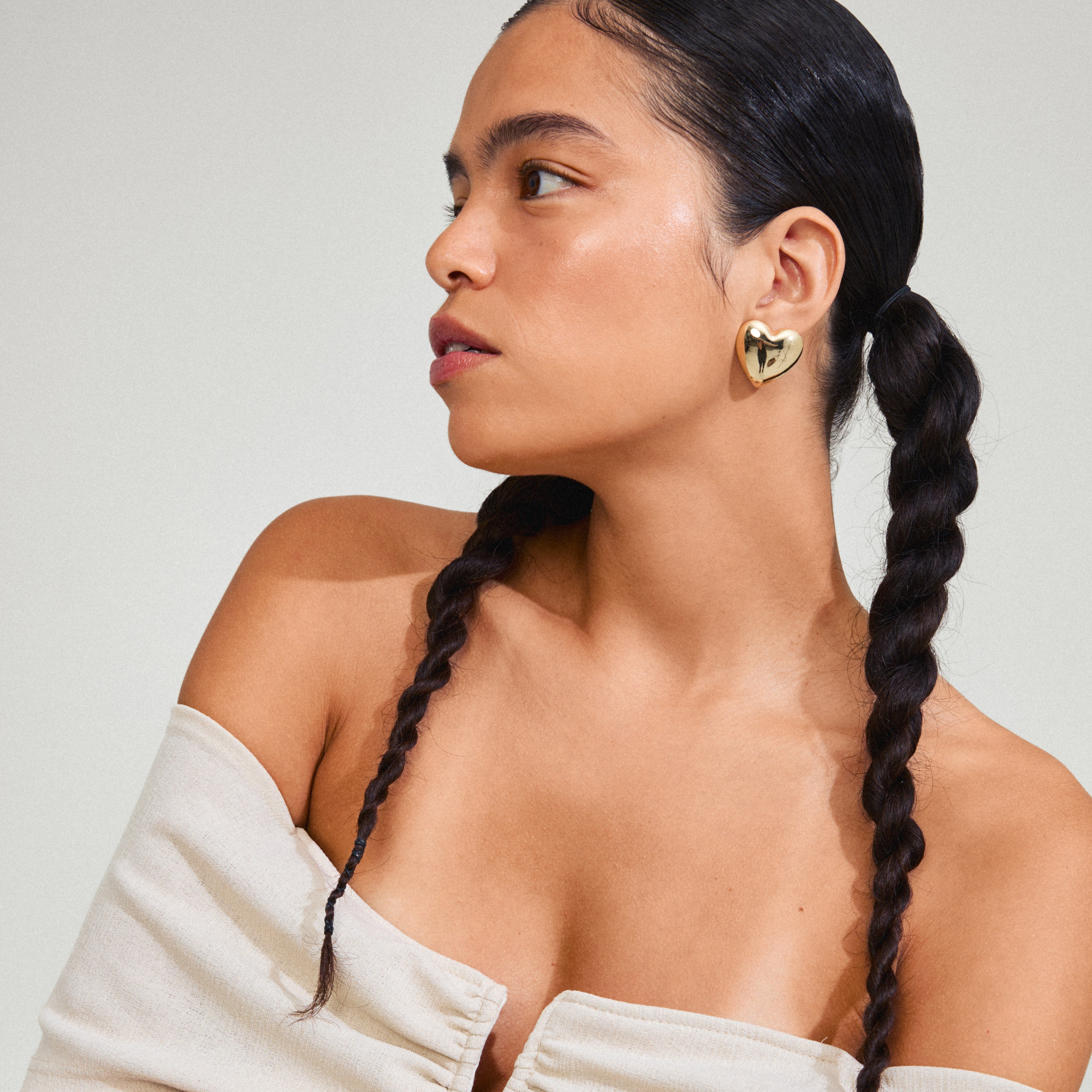 Woman wears ANNEMETTE gold-plated earrings, chunky heart design by Pilgrim, showcasing edgy, romantic style. Perfect for outfits with a touch of glamour.