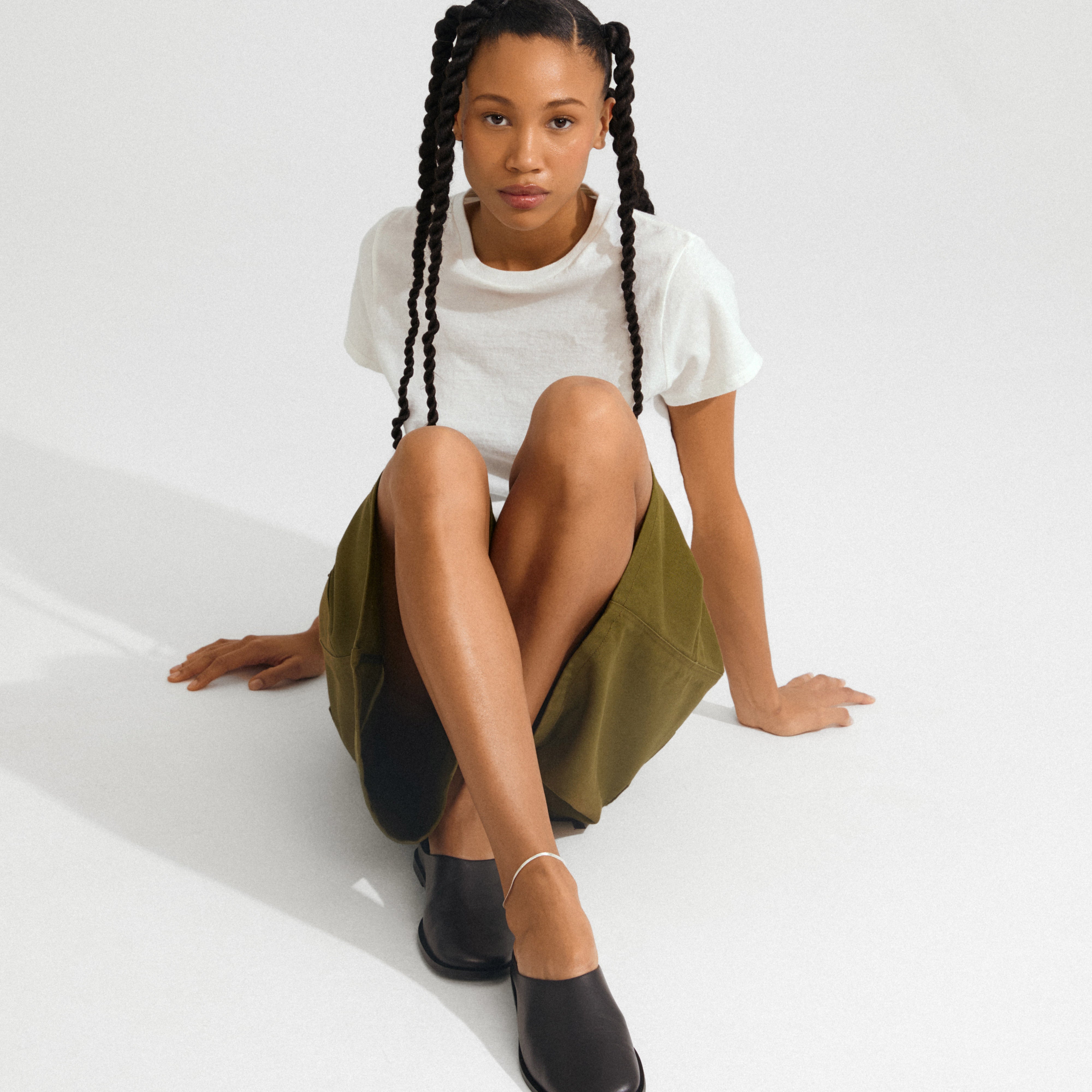 Young person wearing a silver-plated JOANNA anklet, styled with minimalist black slip-ons and an olive skirt, highlighting its elegant, light-reflecting herringbone chain design.