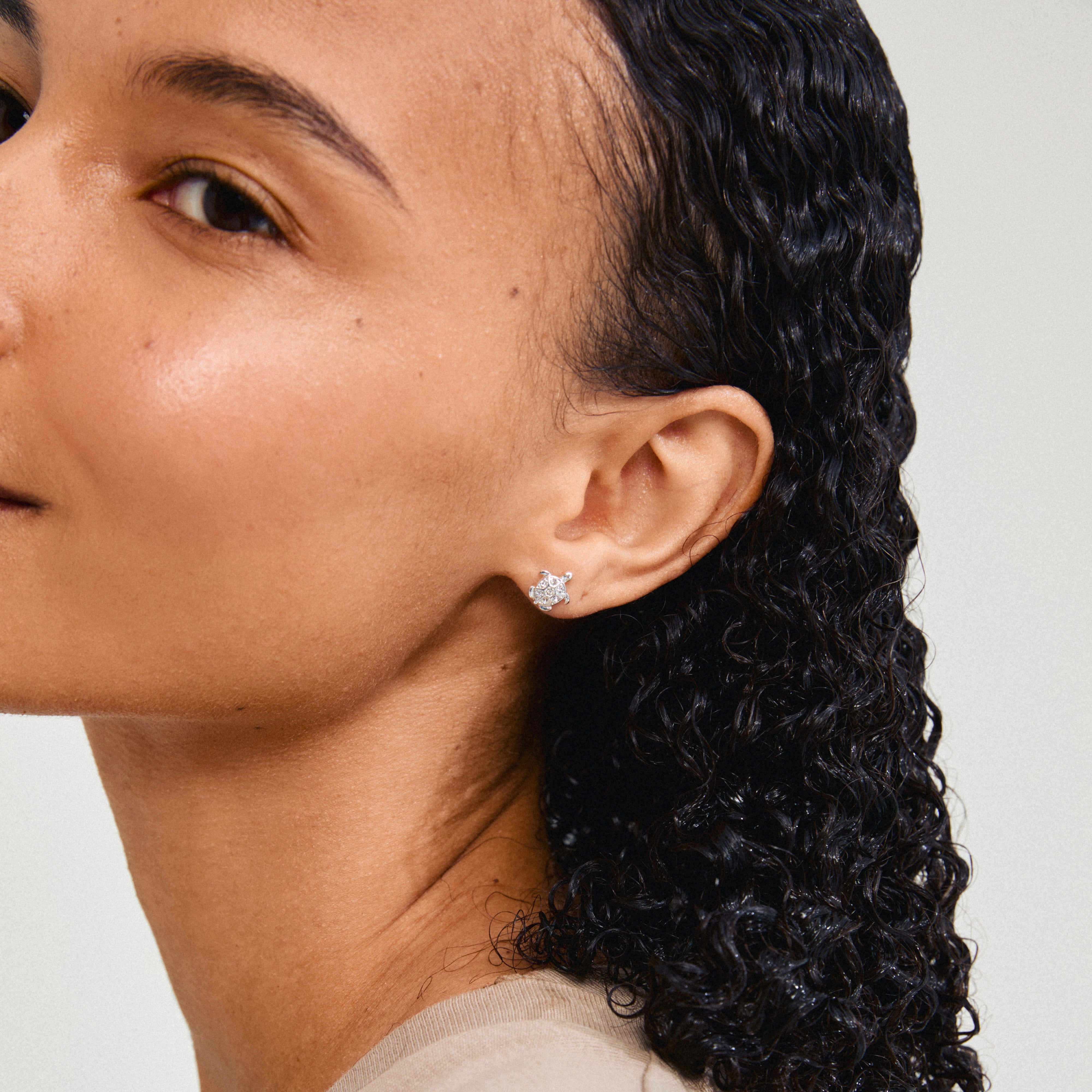 Close-up of a woman's ear showcasing Pilgrim's silver-plated ARCHER earrings with sparkling crystals and turtle design, symbolizing nature's beauty.