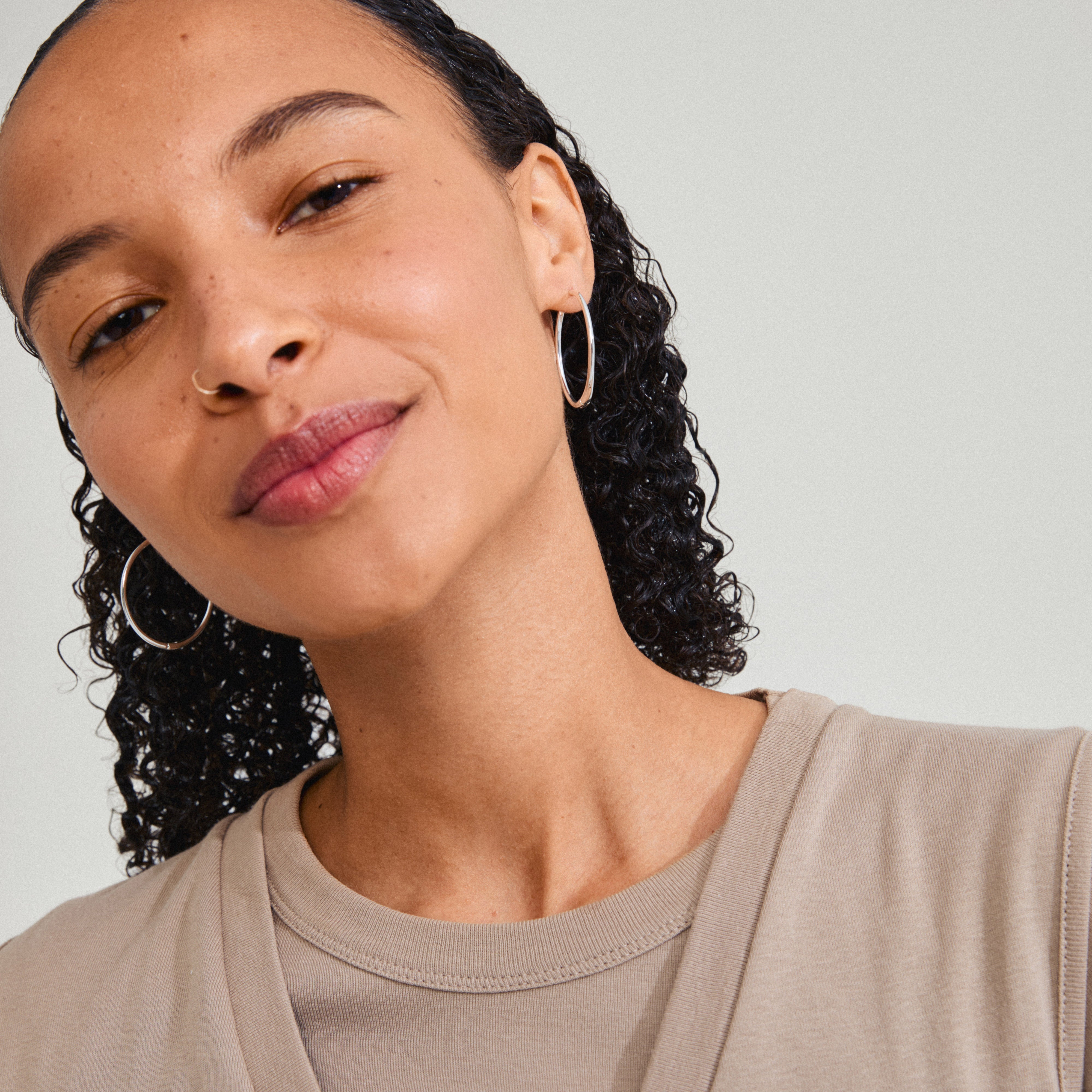 Woman wearing ARTEMIS silver-plated hoop earrings, smiling for a selfie, showcasing their Scandinavian-inspired design and shiny finish, ideal for versatile styling.