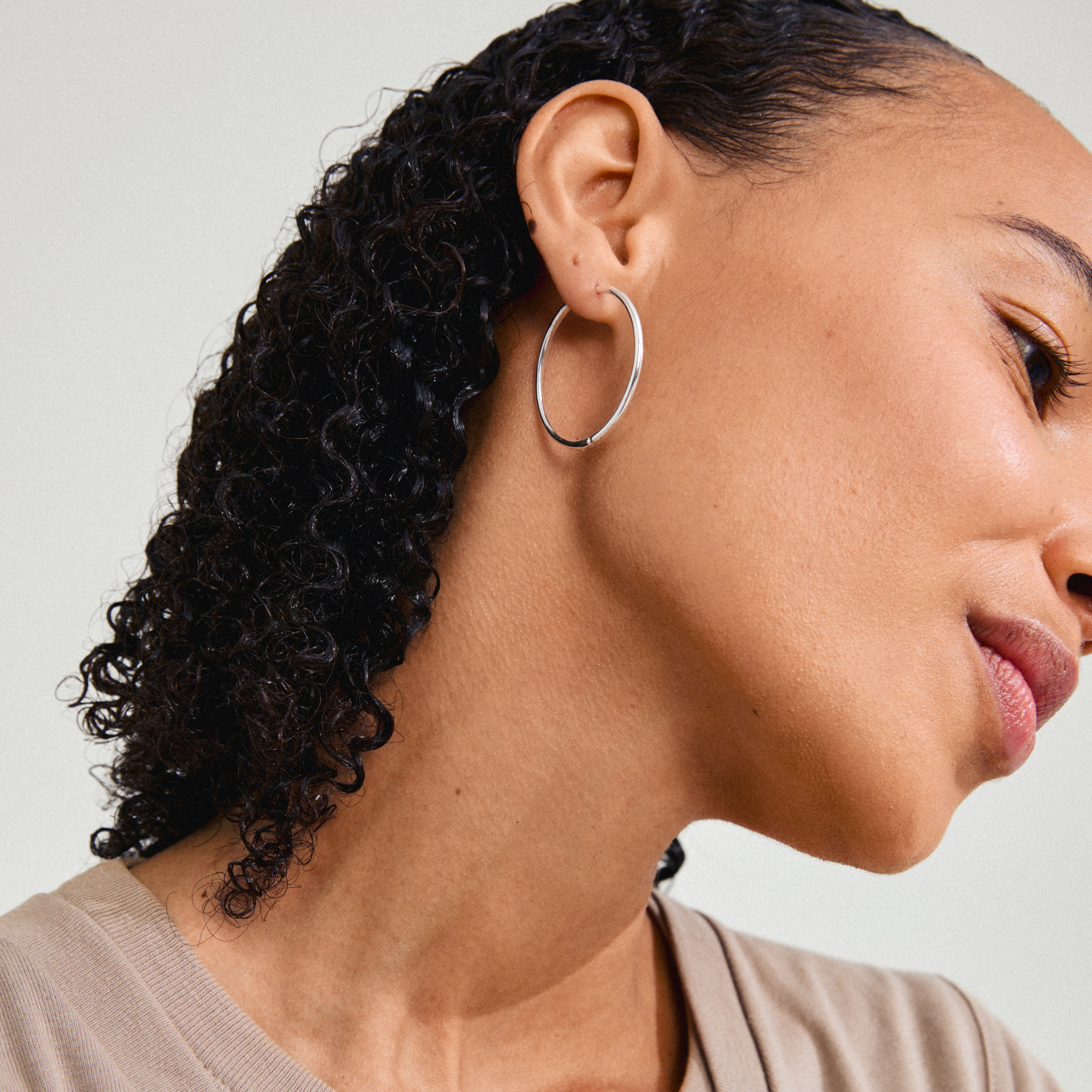 Close-up of a woman wearing Pilgrim's silver-plated ARTEMIS hoop earrings, showcasing their shiny, classic Scandinavian-inspired design.