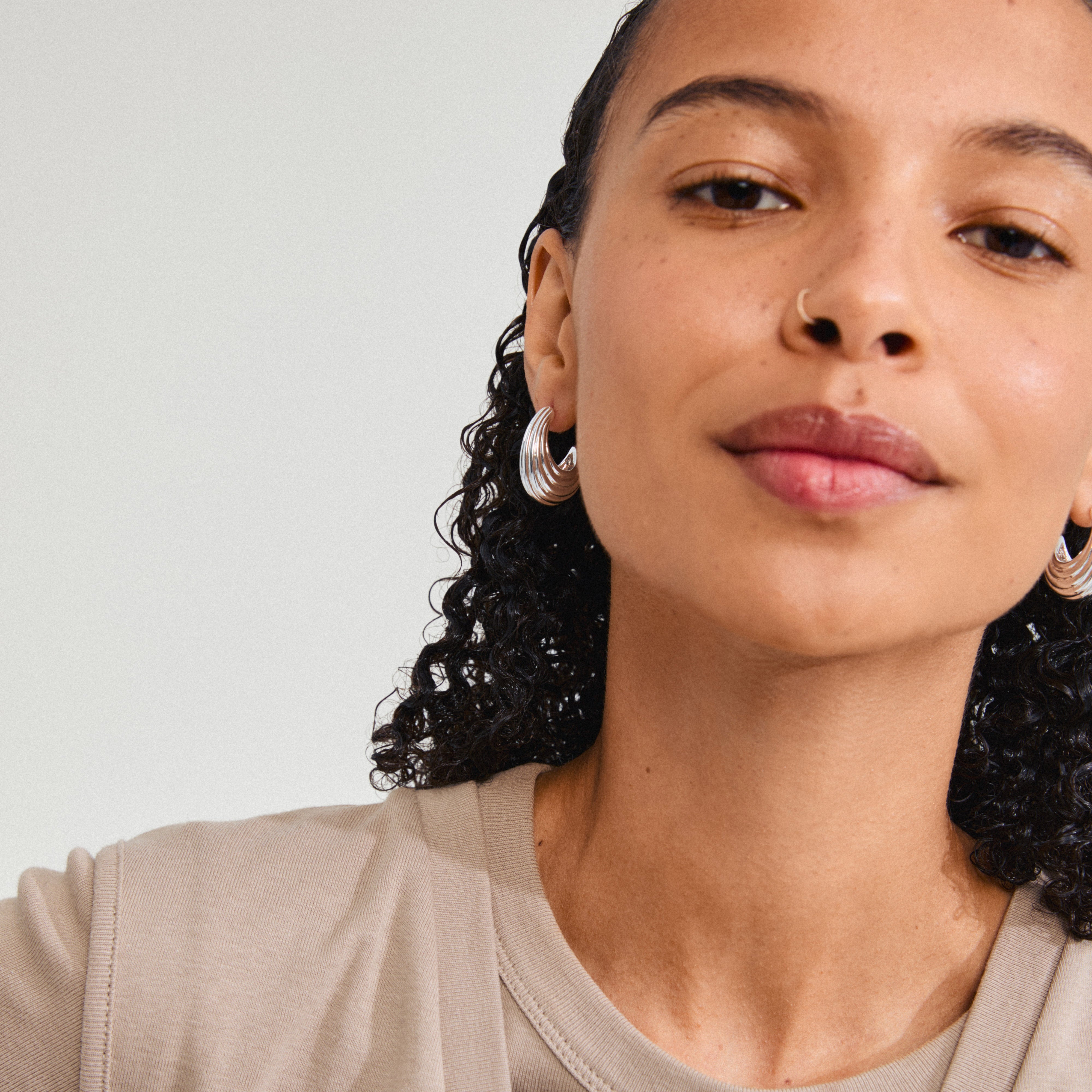 ASLE earrings silver-plated, featuring chunky, fluted half hoops with ocean-inspired design, worn by a woman with curly hair for a trendy, unique look.