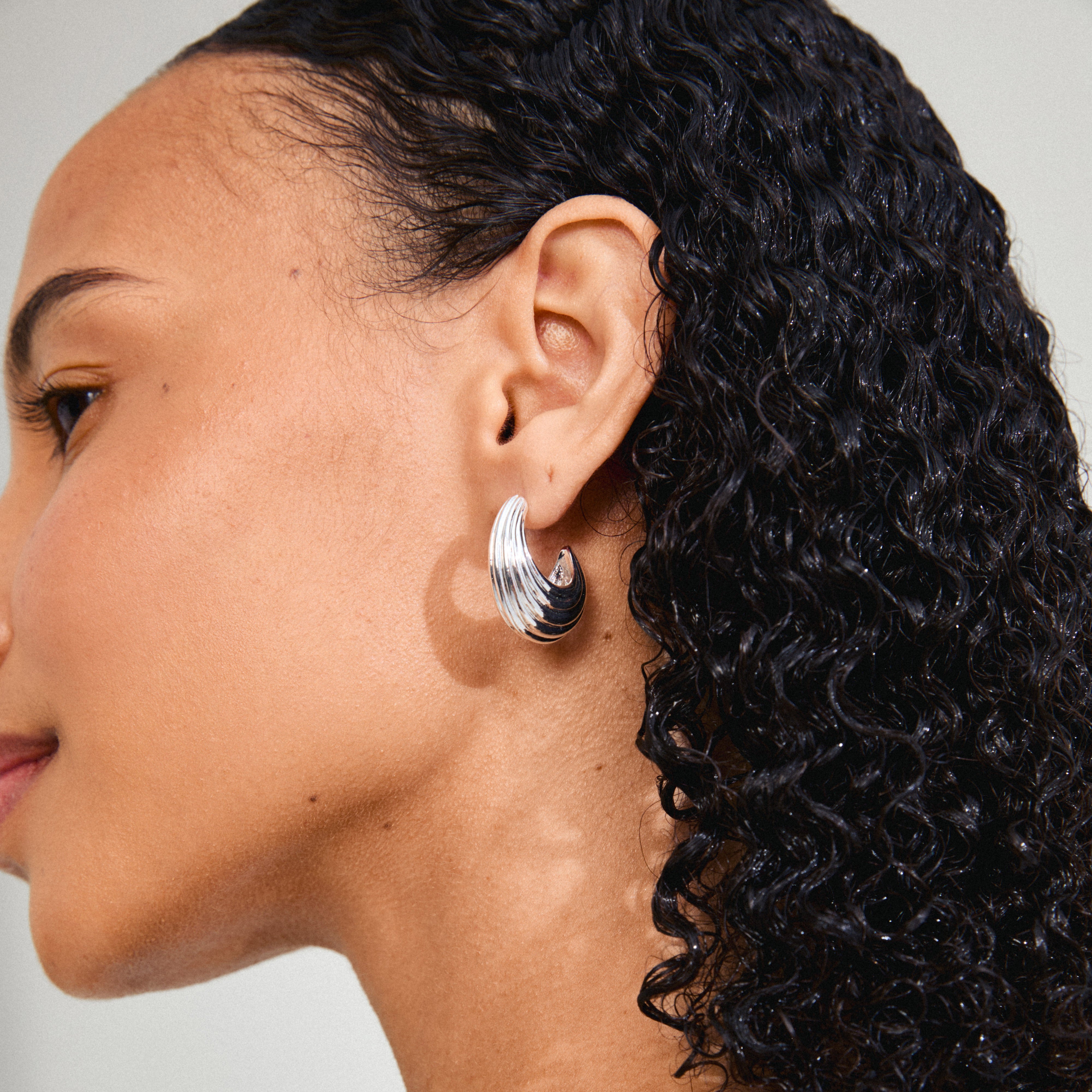 ASLE earrings silver-plated, featuring chunky, fluted textures, worn by a woman with curly hair, highlighting Pilgrim's stylish, retro-inspired design.