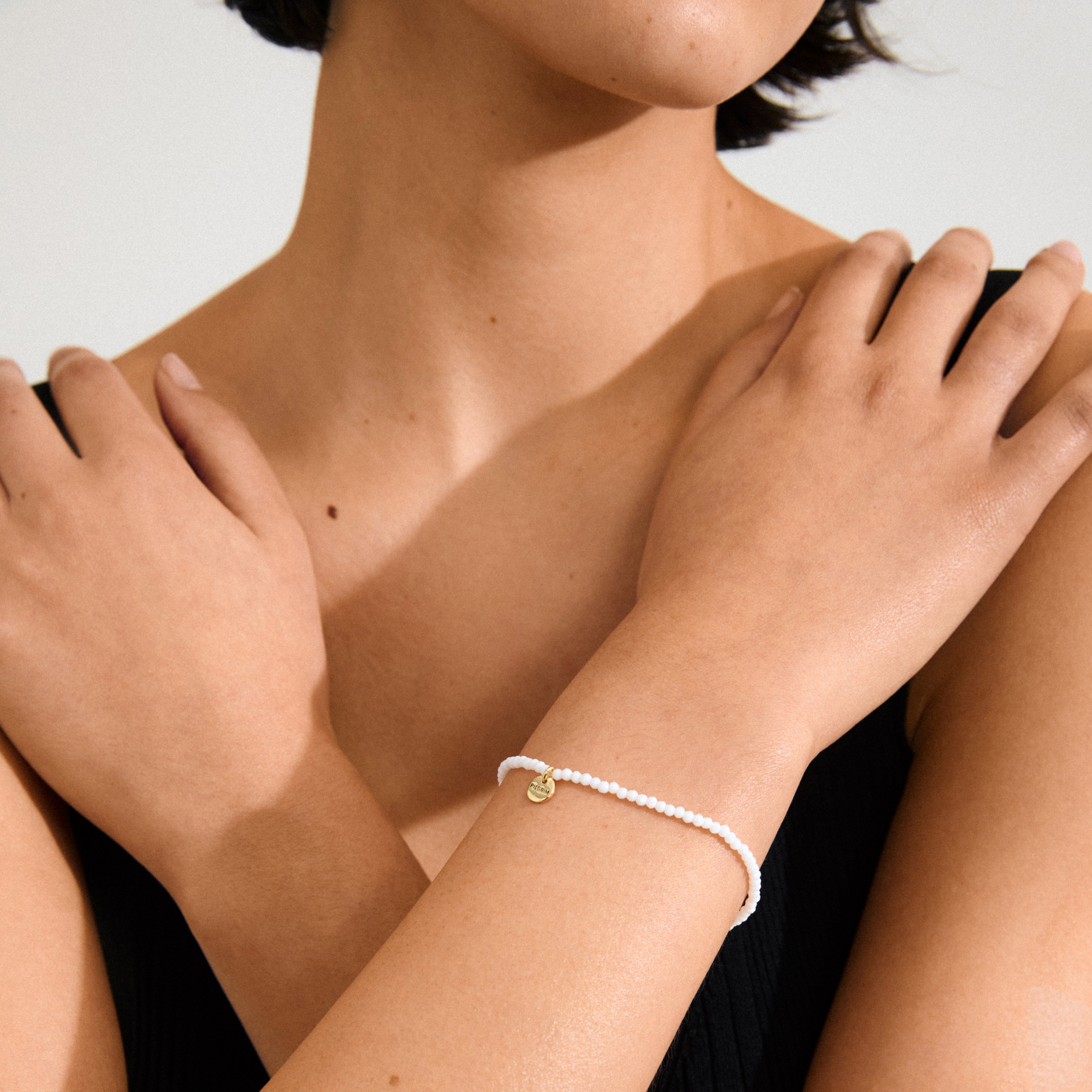 Woman showcasing the INDIE bracelet with white faceted glass beads and gold-plated details, highlighting its elegance and versatility for stacking.