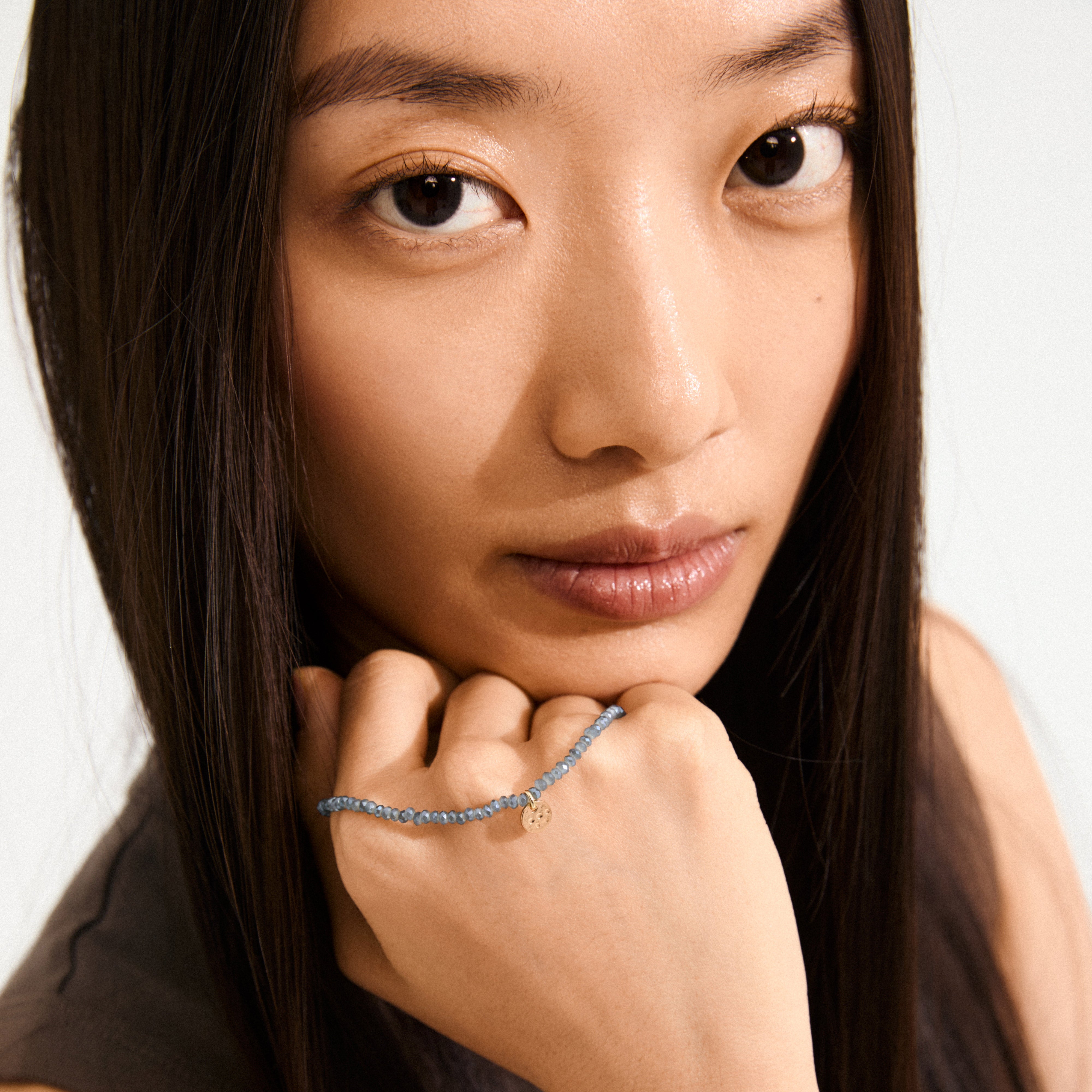 Woman wearing the INDIE bracelet with dusky blue faceted glass beads and a gold-plated logo, highlighting its elegance and versatility for any occasion.