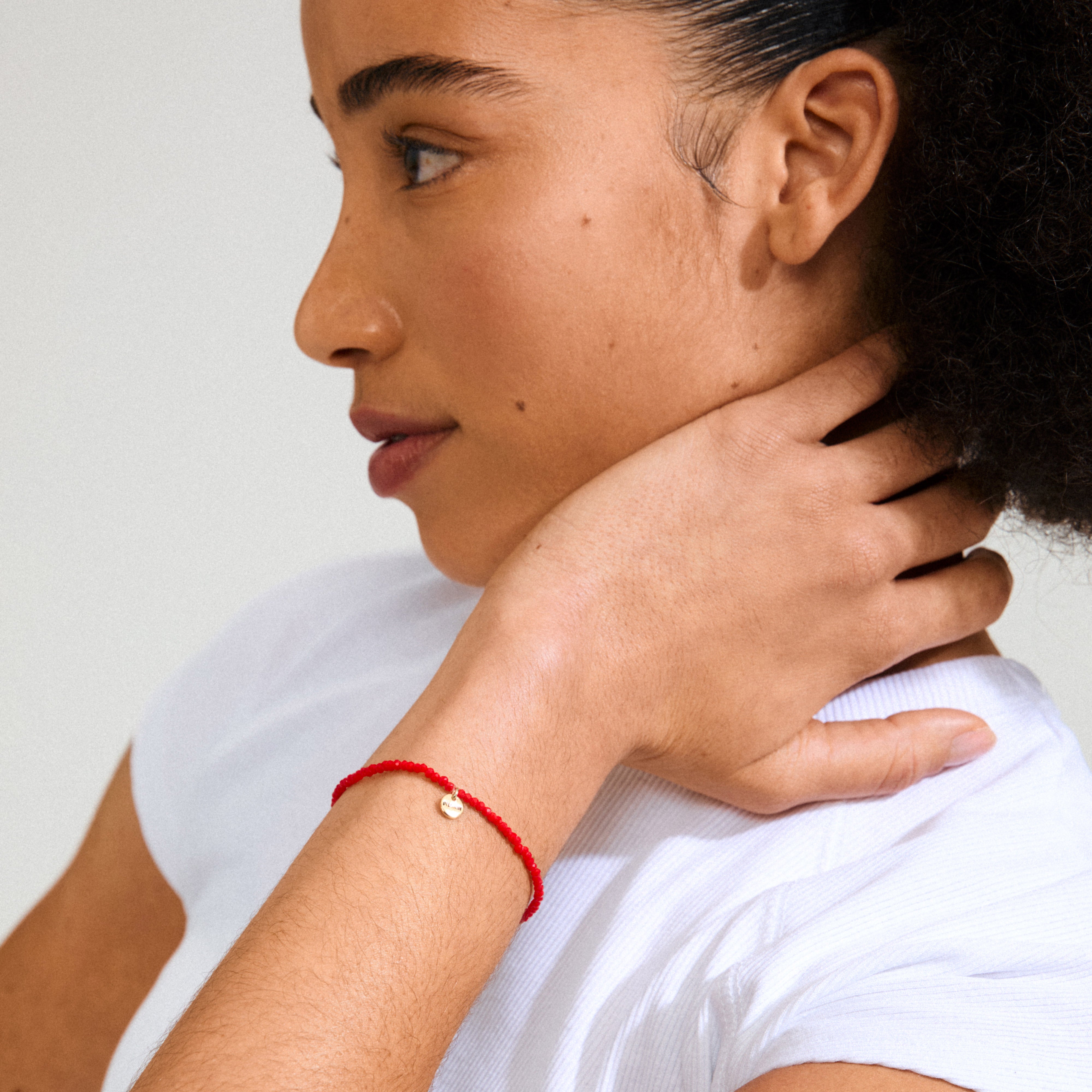 INDIE bracelet red, gold-plated on woman's wrist, showcasing red faceted glass beads and gold-plated logo, perfect for stacking and everyday wear.