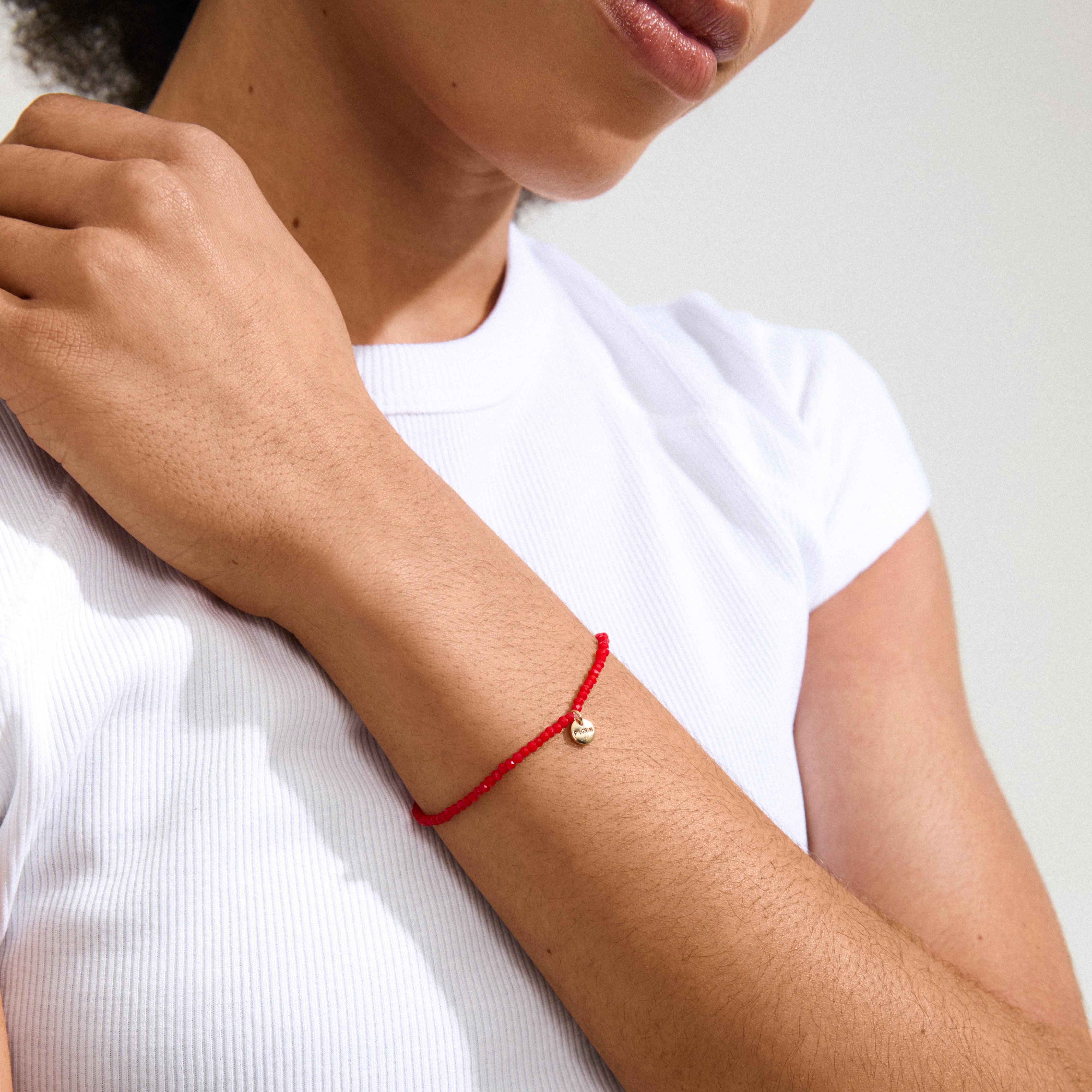 INDIE bracelet in red with gold-plated logo on a woman's wrist, featuring faceted glass beads and elastic fit, perfect for stylish accessorizing.