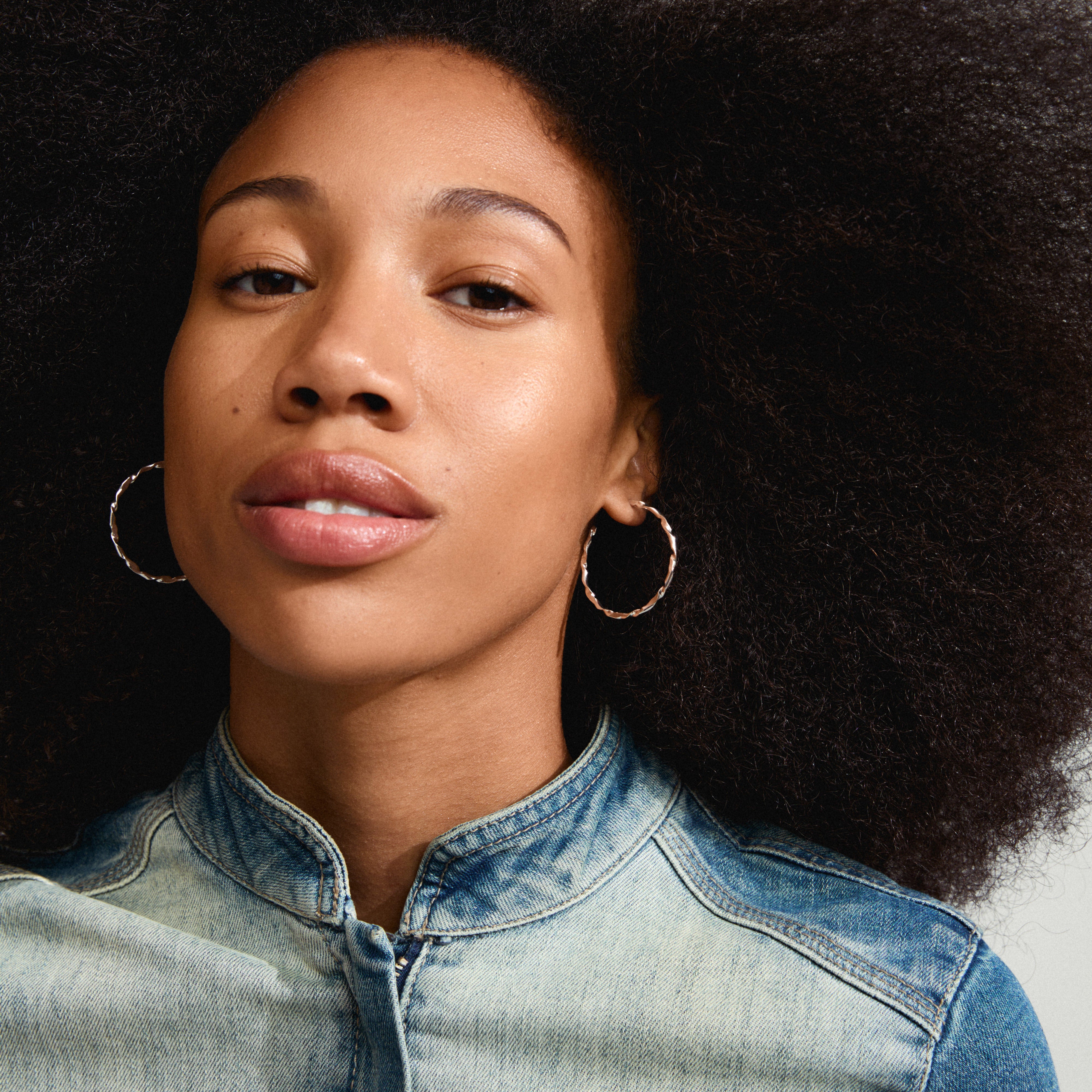 Close-up of a woman wearing WYATT silver-plated hoop earrings, showcasing their sleek, wavy design. Perfect for both daily wear and special occasions.