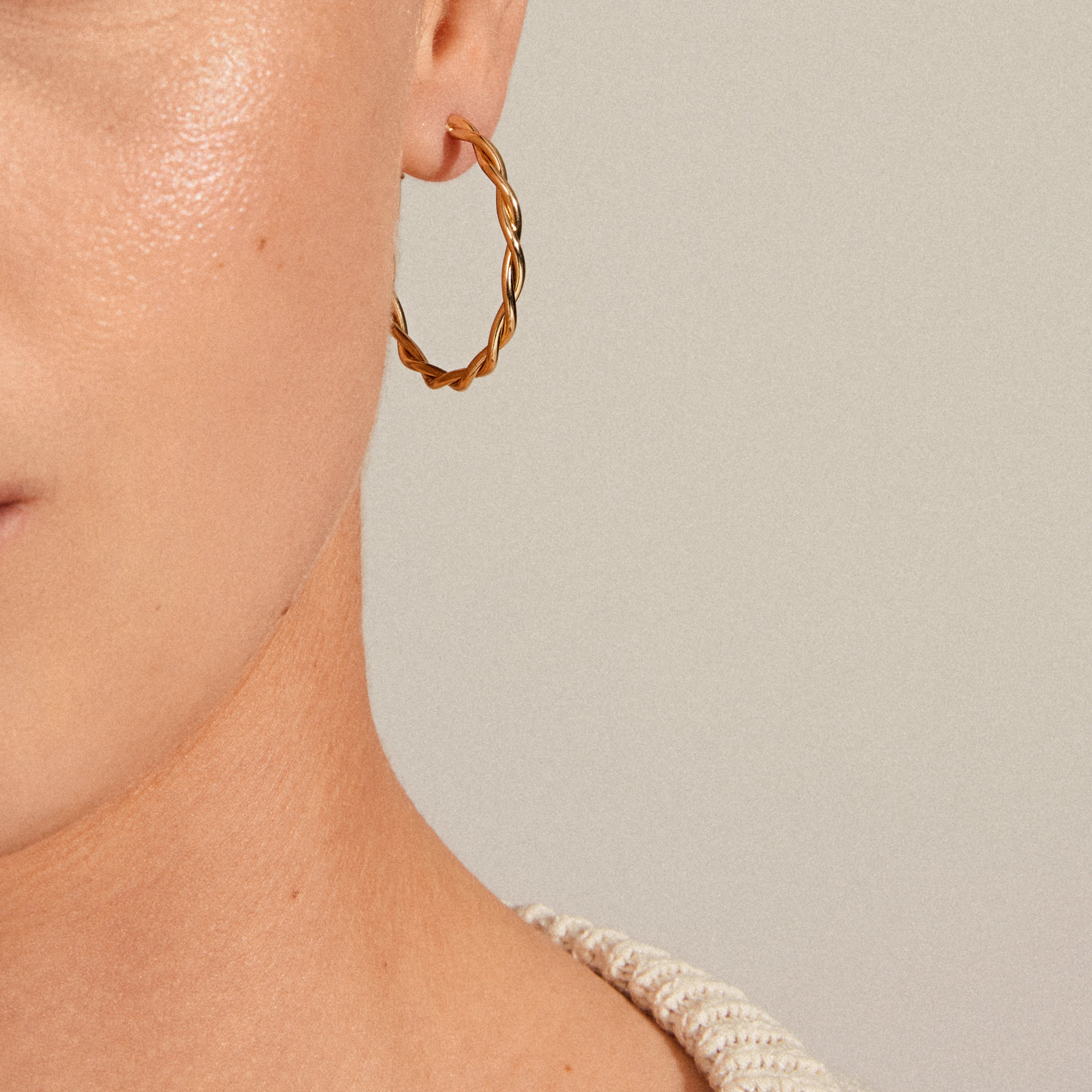 Close-up of a person's ear wearing NAJA large gold-plated twisted hoop earrings, highlighting the stylish design and reflective quality of the medium-sized hoops.