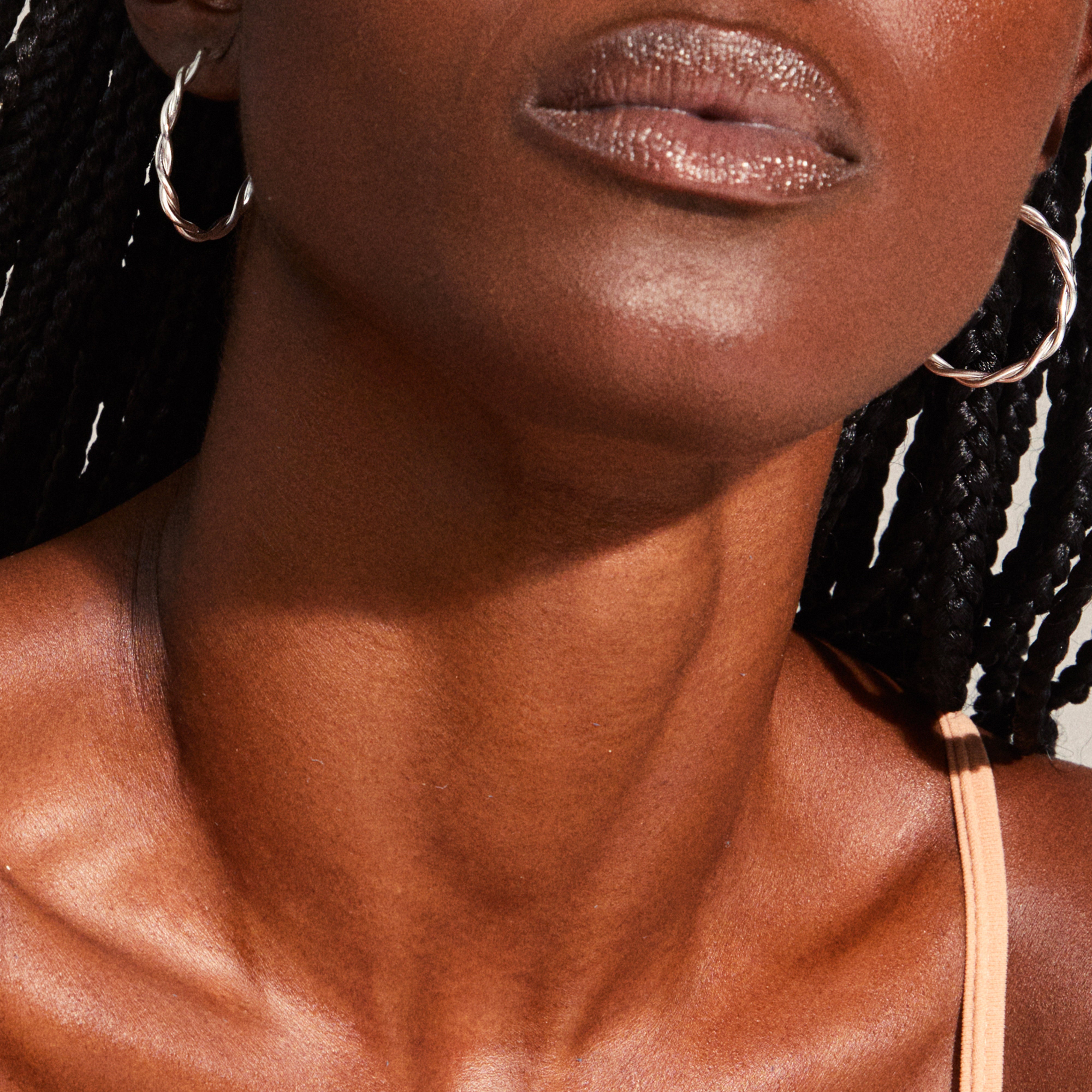 Close-up of a person's lower face wearing Pilgrim's NAJA large, twisted silver-plated hoop earrings, highlighting the elegant design and reflective light effects.
