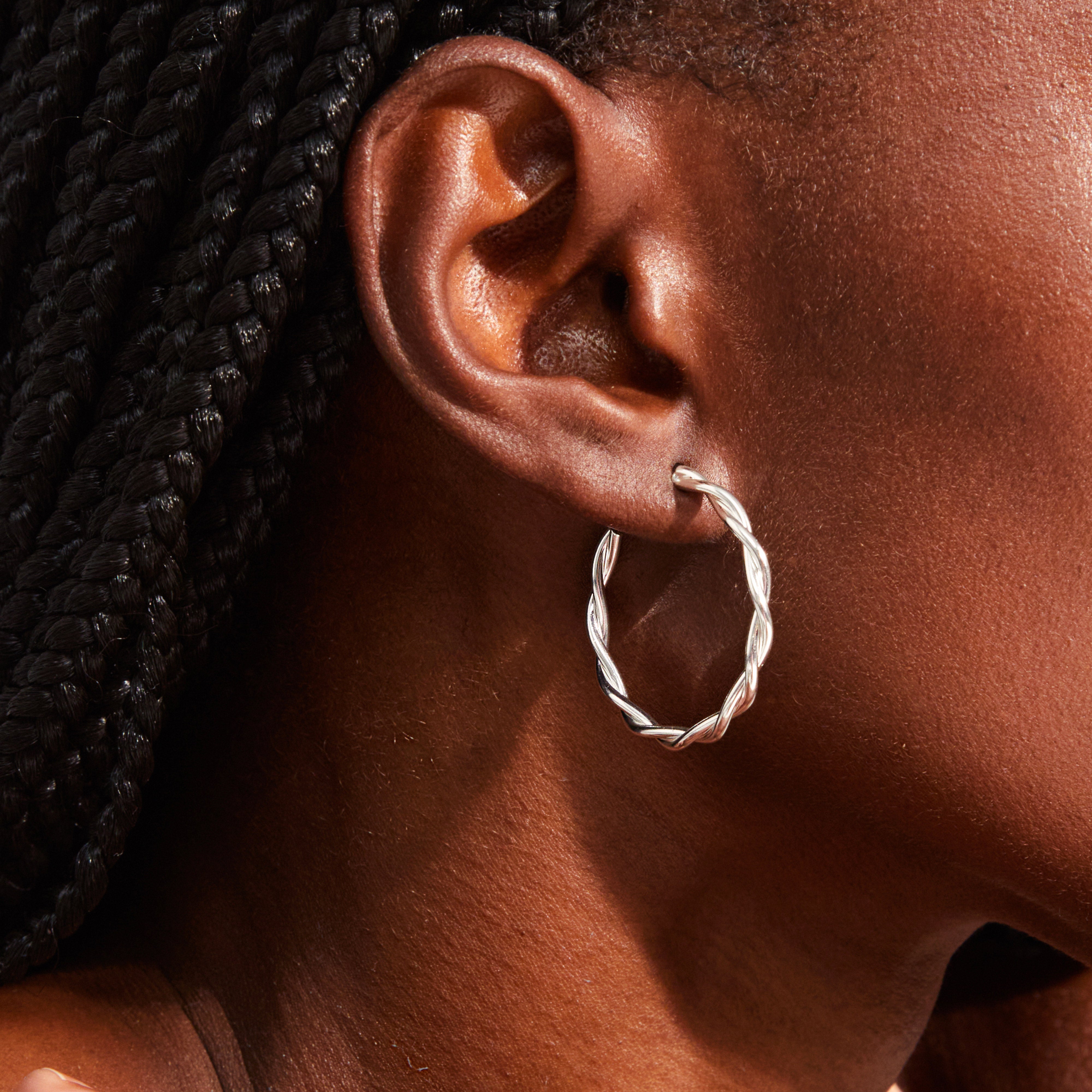 Close-up of an ear adorned with NAJA large silver-plated twisted-wire hoop earring, showcasing its chic design and light-reflecting twists.