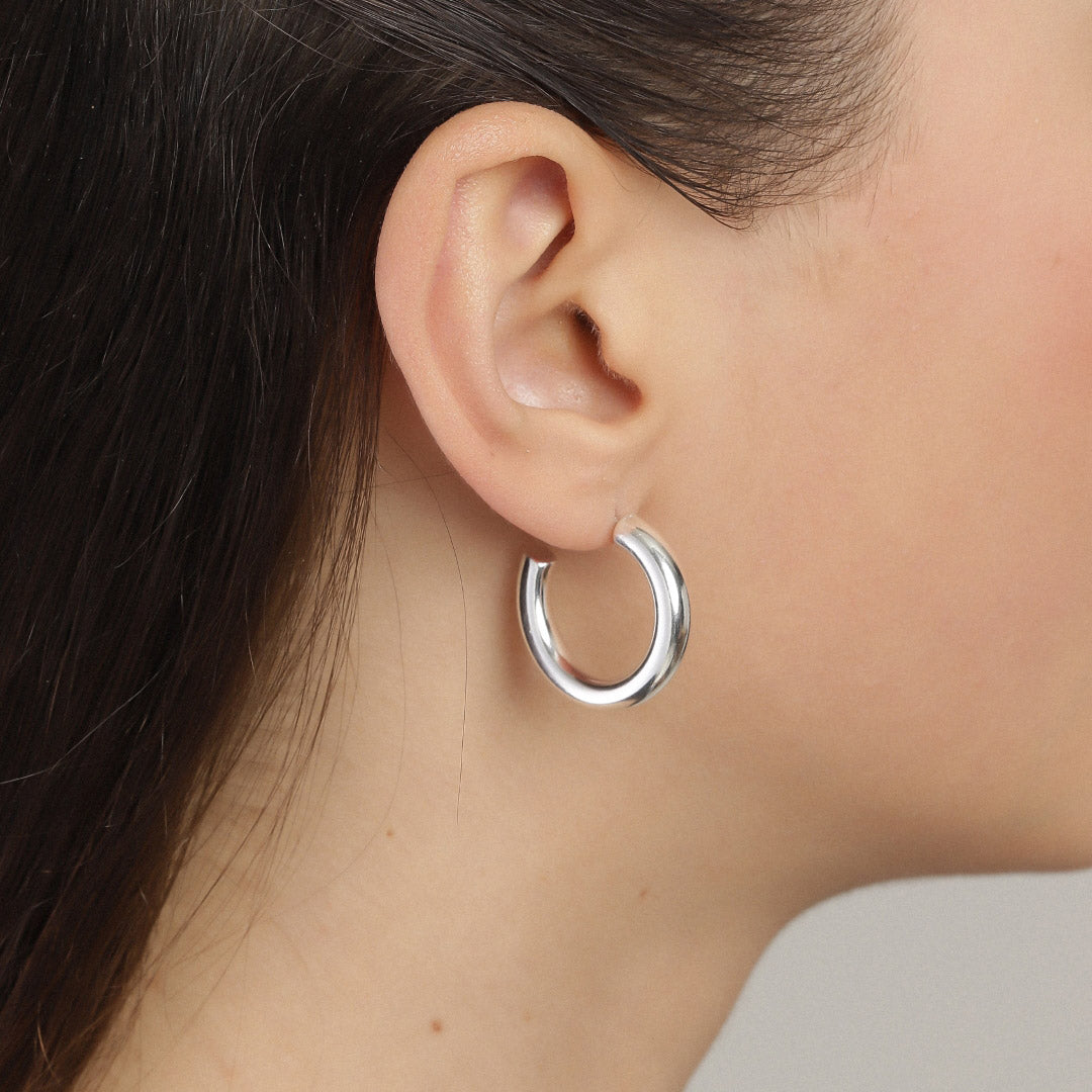 Silver-plated MADDIE chunky hoop earring shown on a woman's ear, highlighting its shiny, stylish design perfect for both casual and elegant outfits.