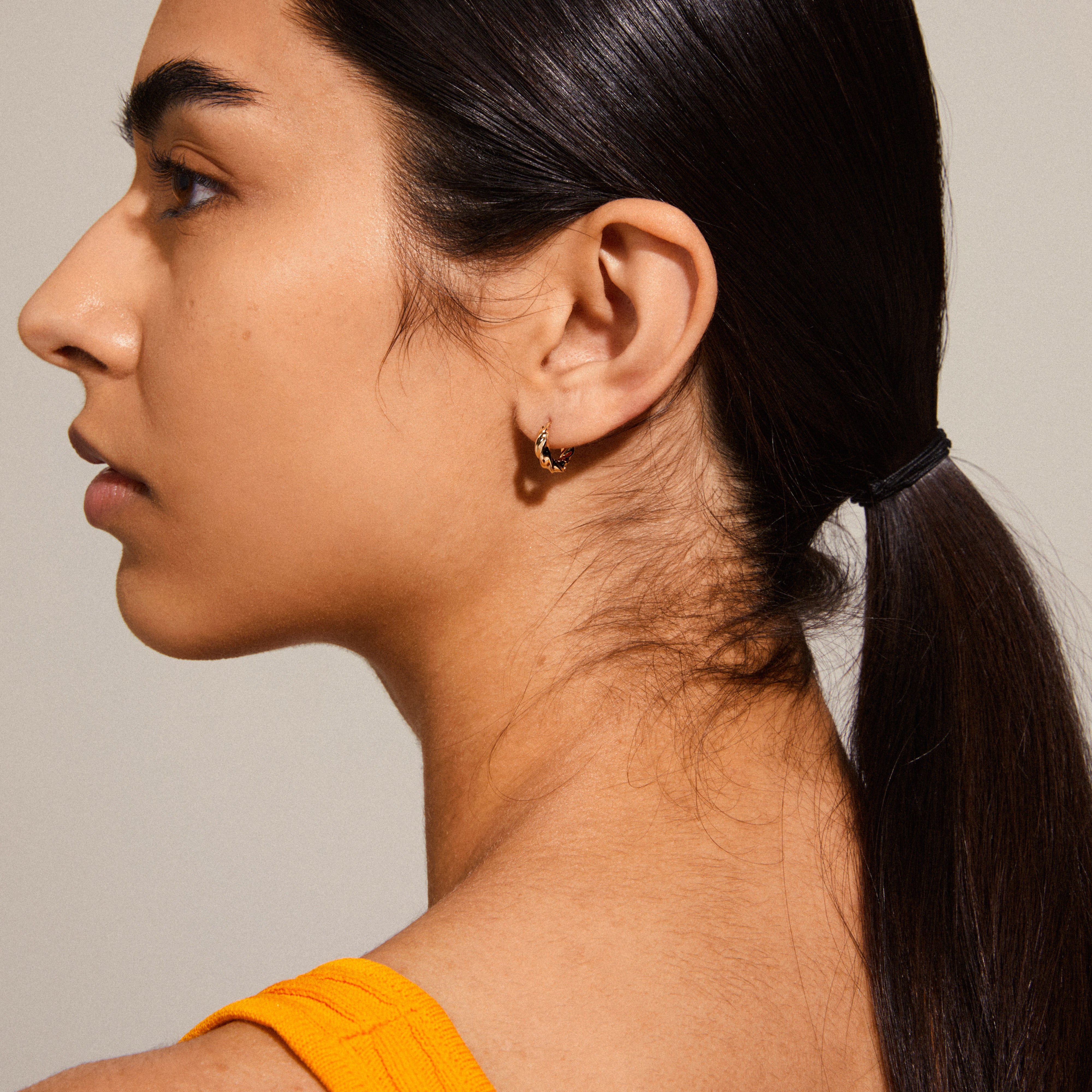 TAFFY small swirl hoop earrings gold-plated adorn a woman's ear, showcasing their organic, handcrafted design inspired by nature's lively shapes.