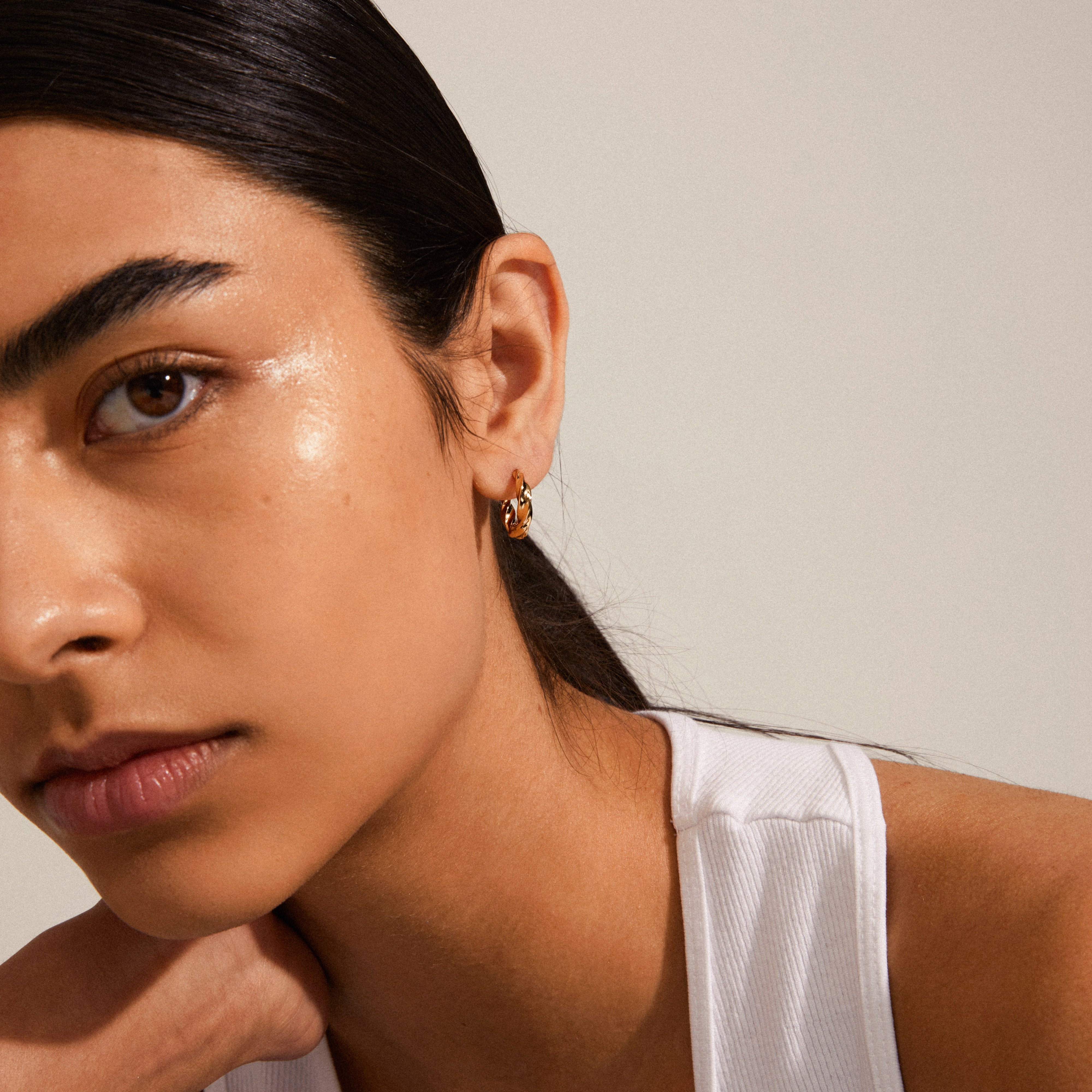 Woman with dark hair wearing a white tank top, showcasing Pilgrim's TAFFY medium size swirl hoop earrings, gold-plated, highlighting their vintage-inspired, feminine design.