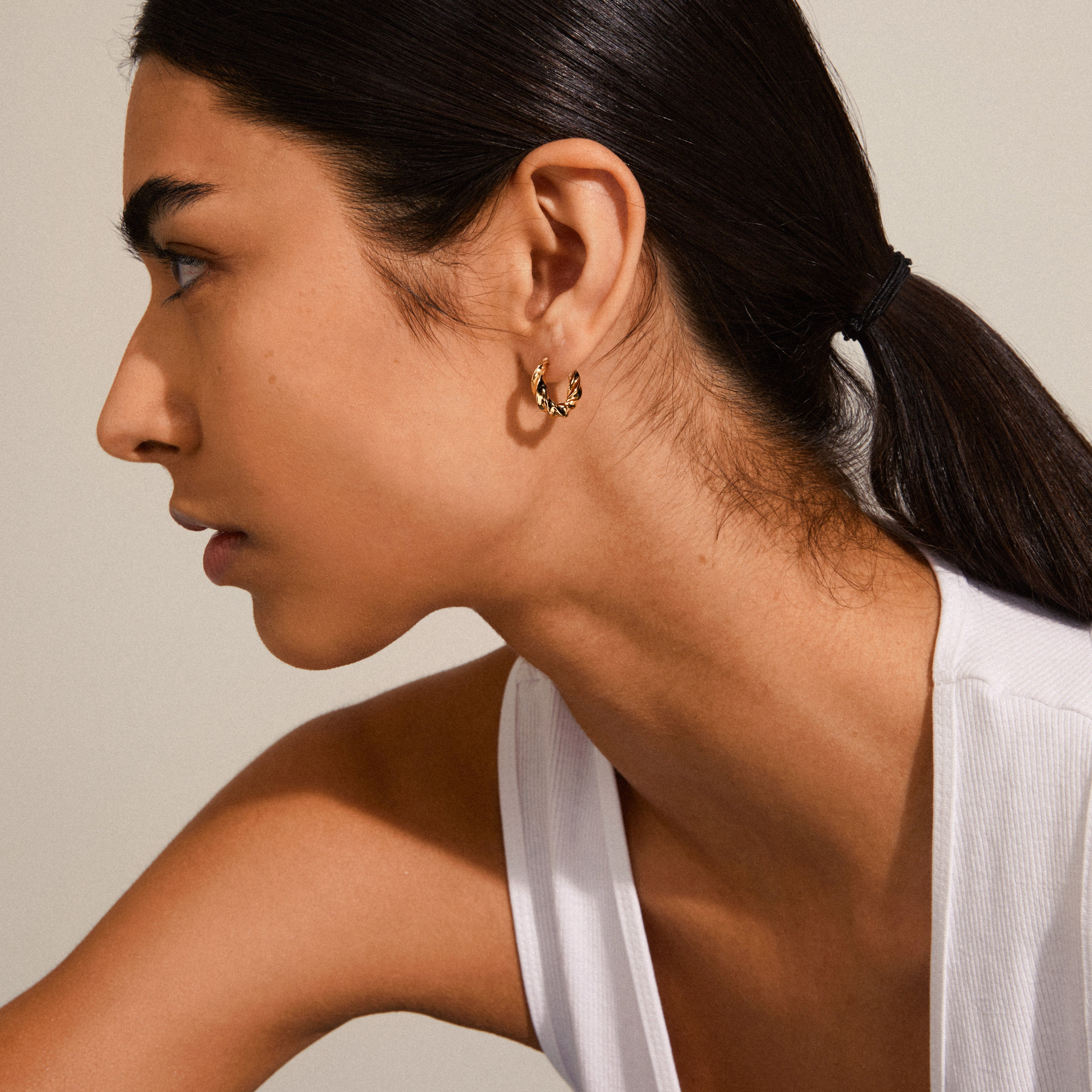 Woman wearing Pilgrim's TAFFY medium size gold-plated swirl hoop earrings, showcasing their elegant and edgy design with a vintage-inspired twist.