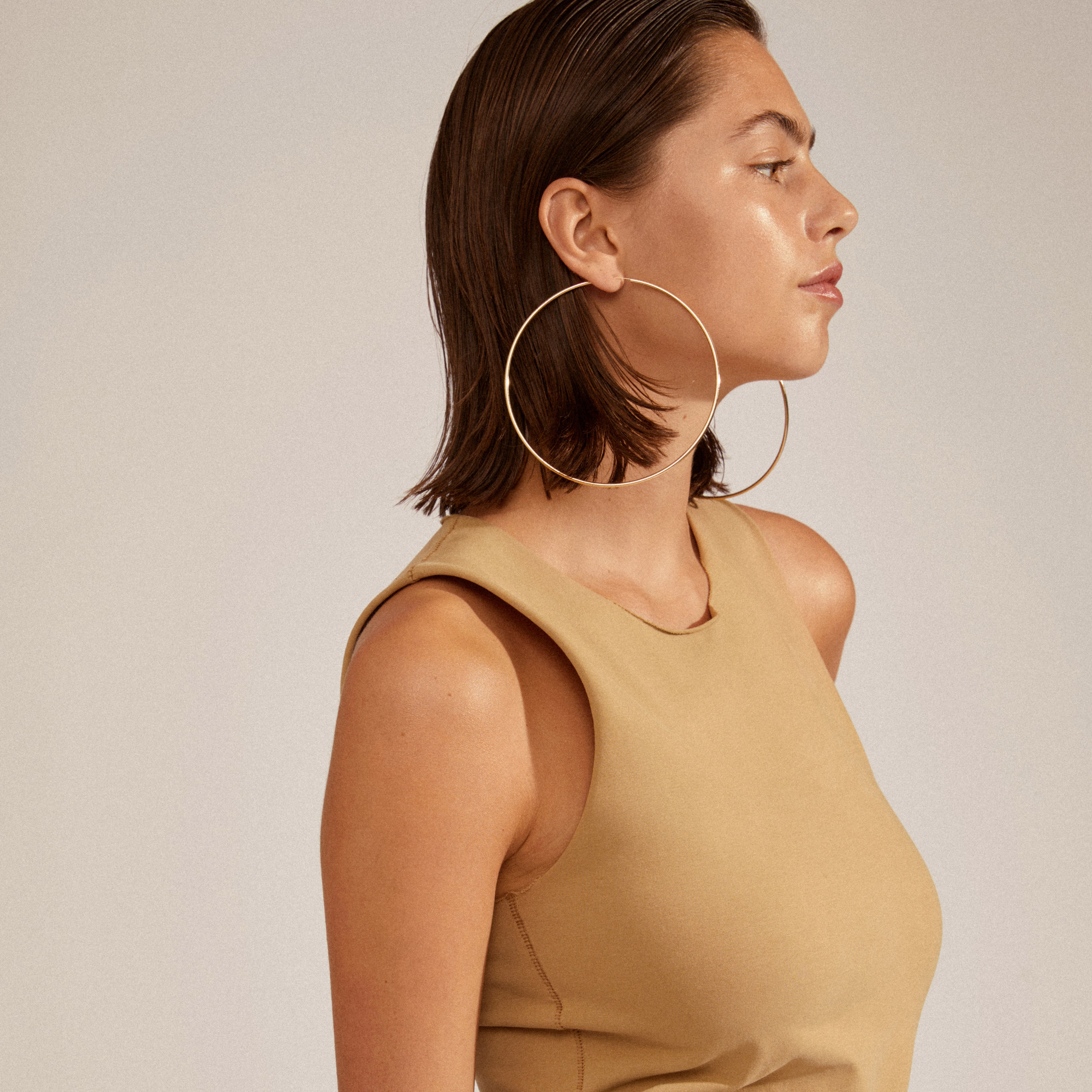 Close-up of APRIL mega hoop earrings, gold-plated, showcasing their large 100mm diameter and elegant design as worn by a person.