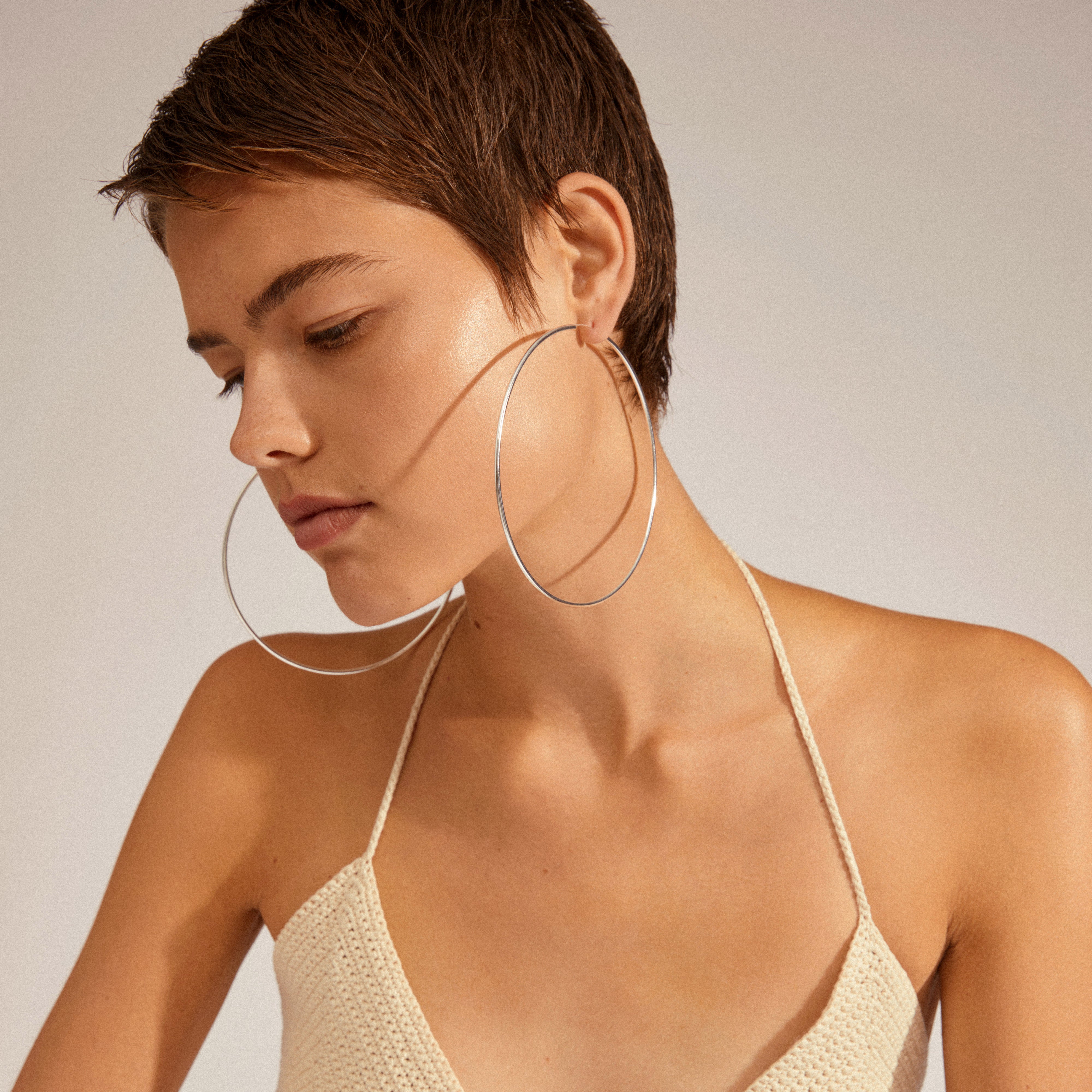 Close-up of a woman wearing APRIL mega hoop earrings, silver-plated, showcasing their 100 mm diameter and elegant, slim silhouette.