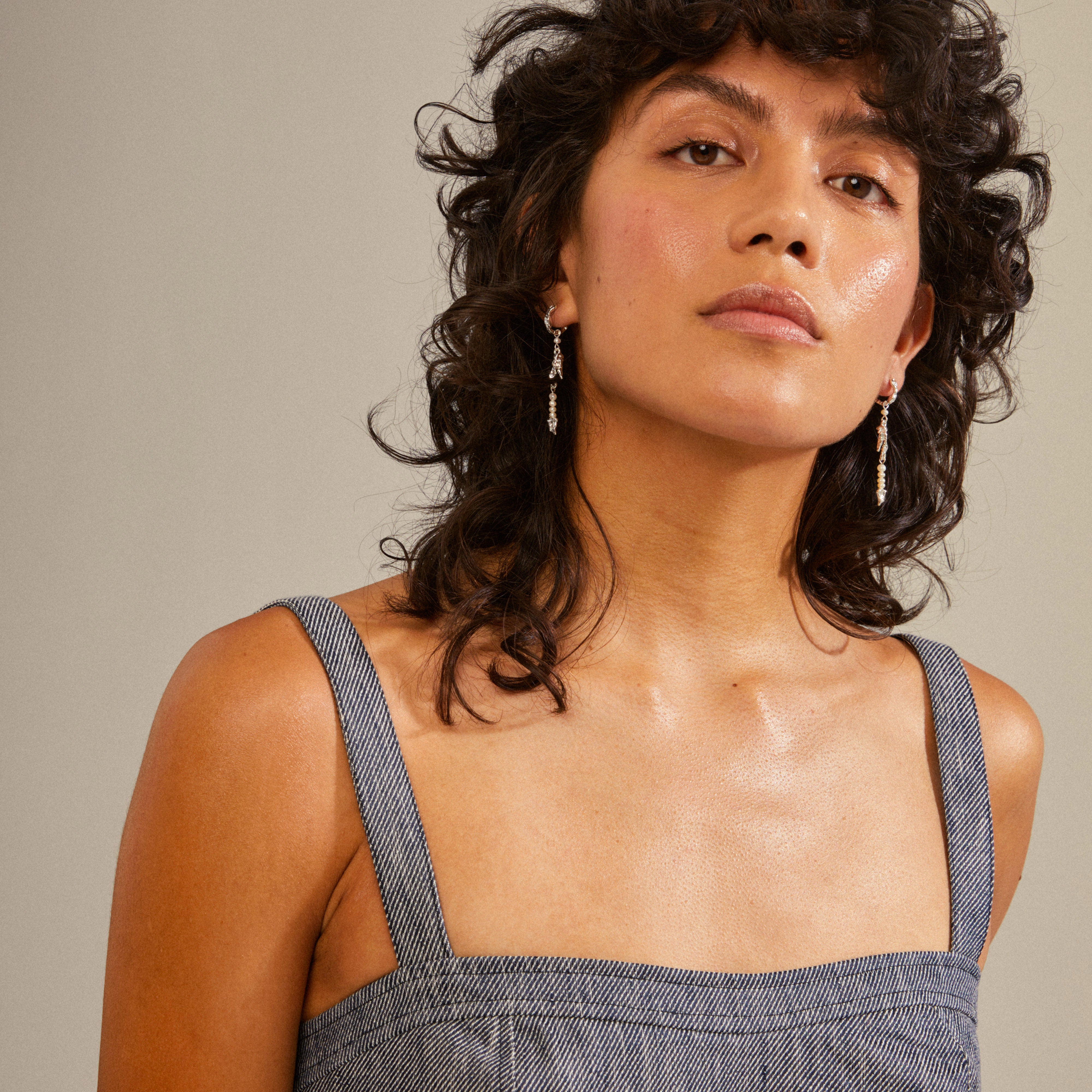 Woman with curly hair wearing NIYA freshwater pearl earrings, silver-plated, featuring organic shapes and genuine pearls, complementing her style.