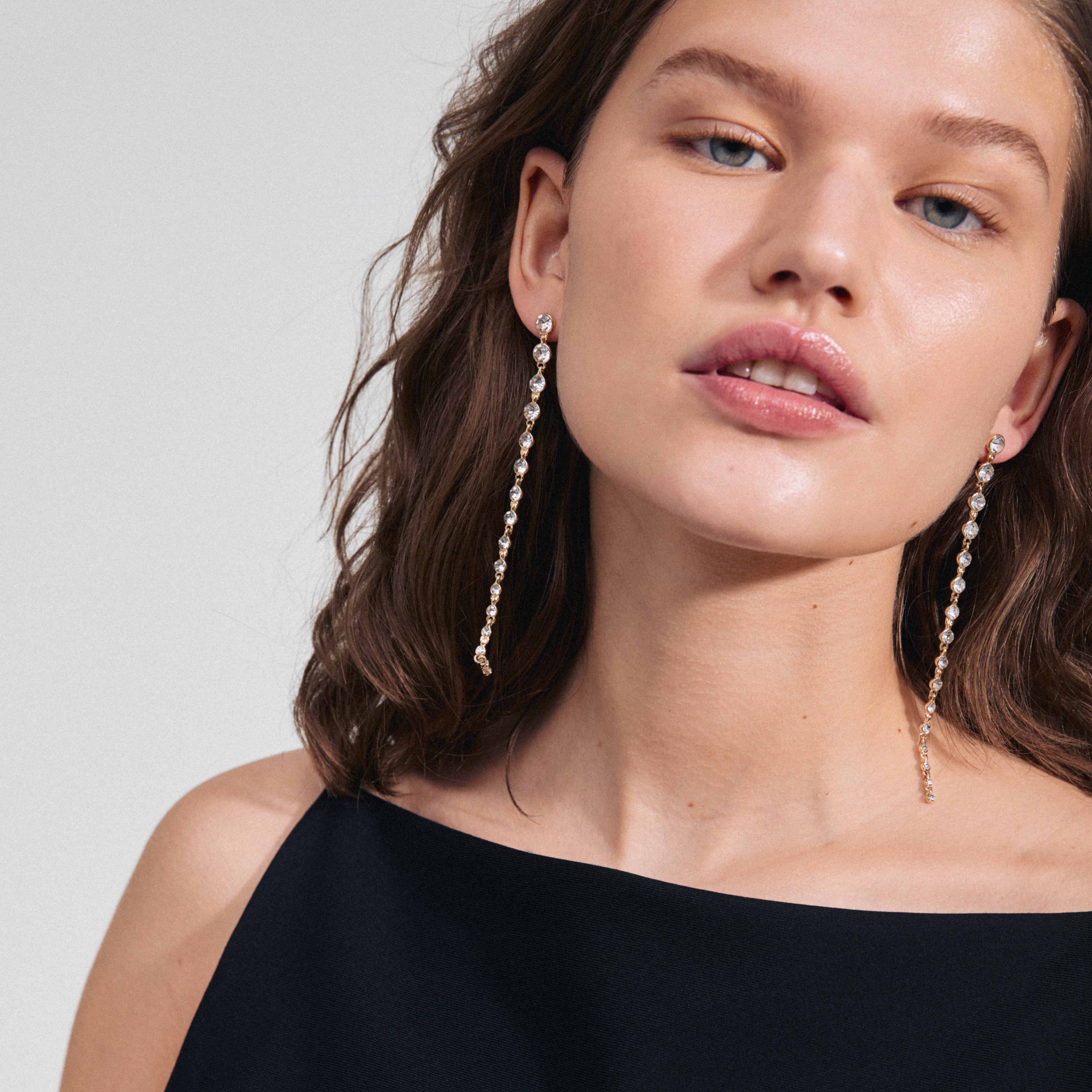 Woman wearing REAGAN crystal earrings, featuring long chains of sparkling Preciosa crystals, designed by Pilgrim for glamorous occasions.