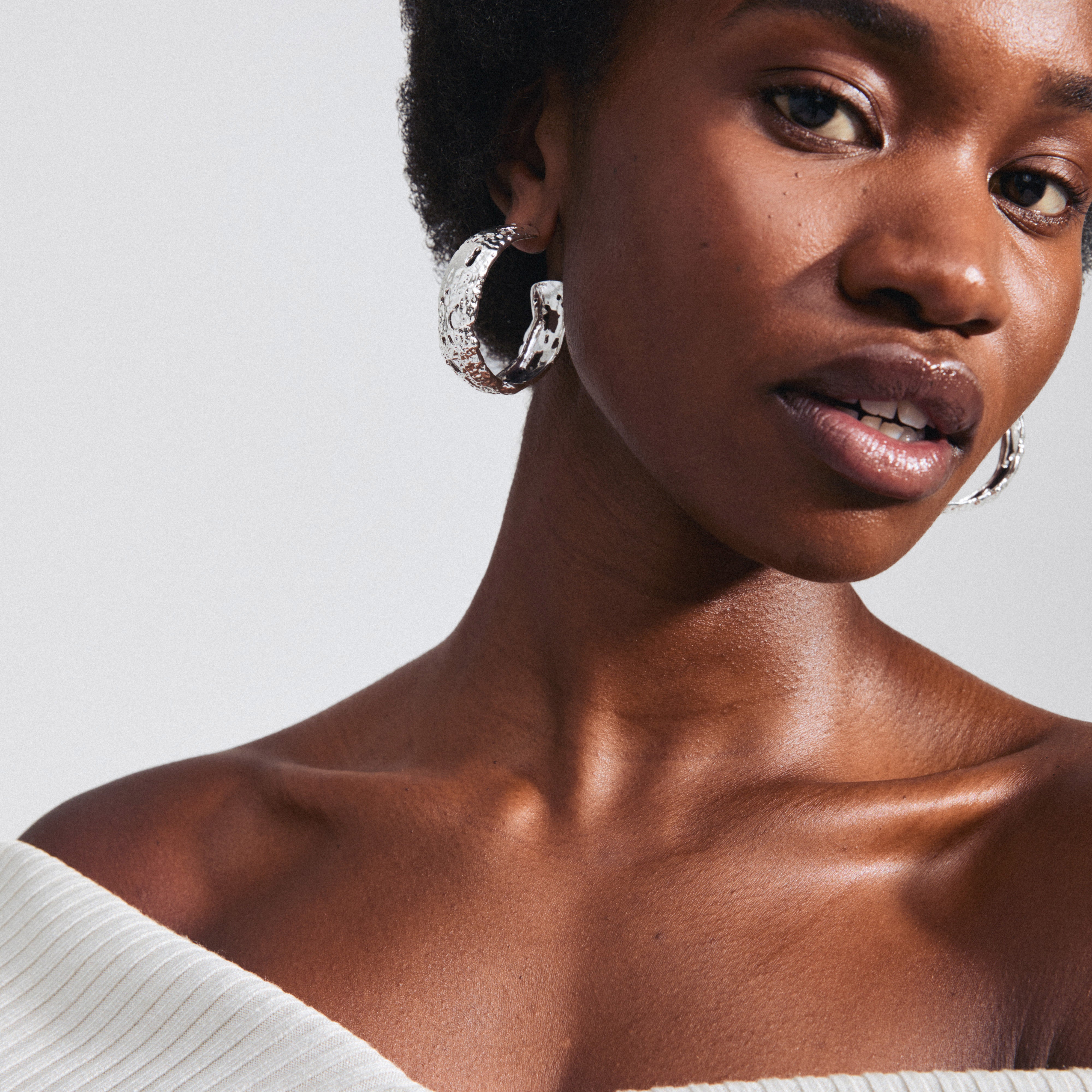 Close-up of a woman wearing large, silver-plated ELENI earrings by Pilgrim, showcasing their rustic, perforated design and bold, wide silhouette.