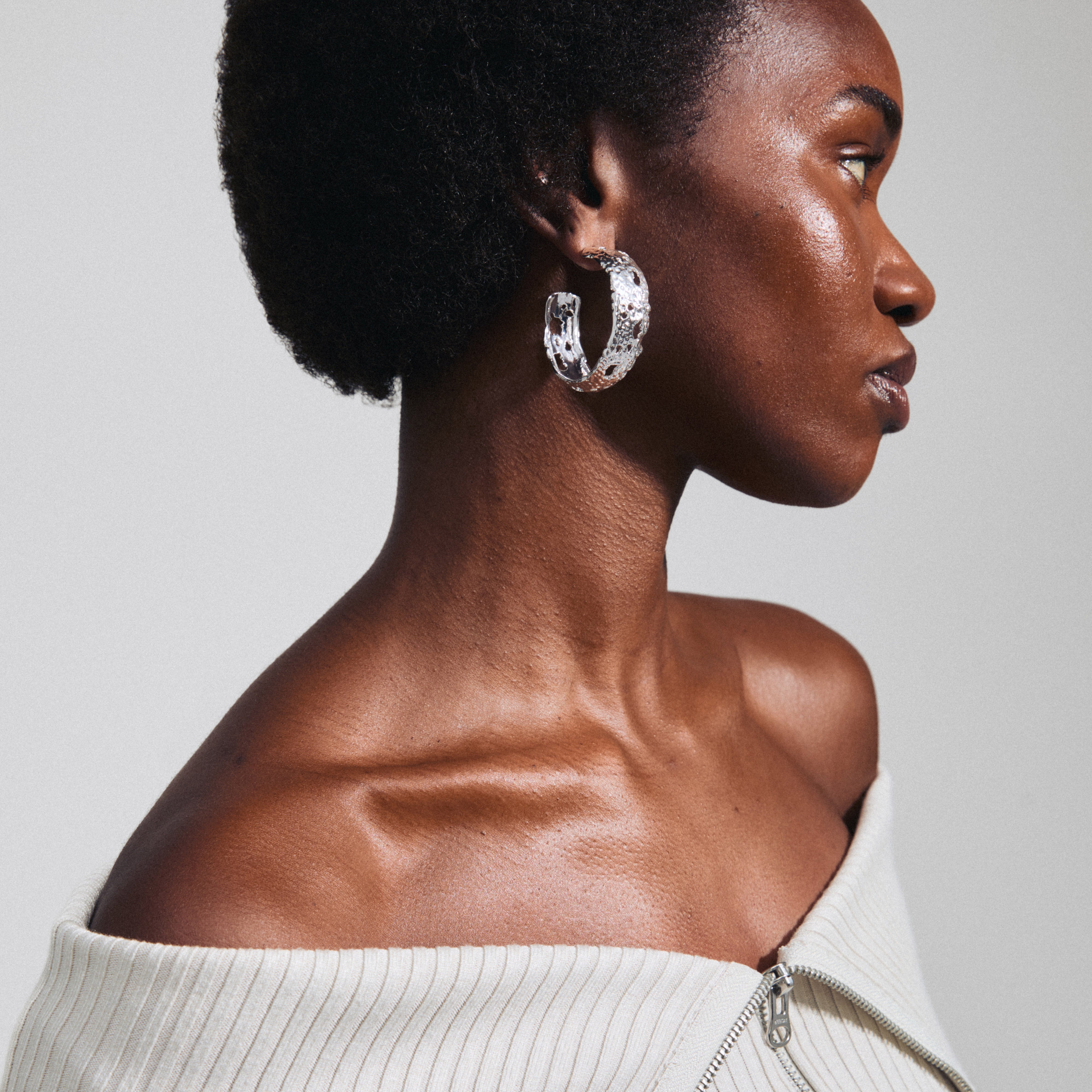 Silver-plated ELENI earrings, featuring large perforated hoops with a rustic design, worn by a woman with short hair, showcasing unique style.