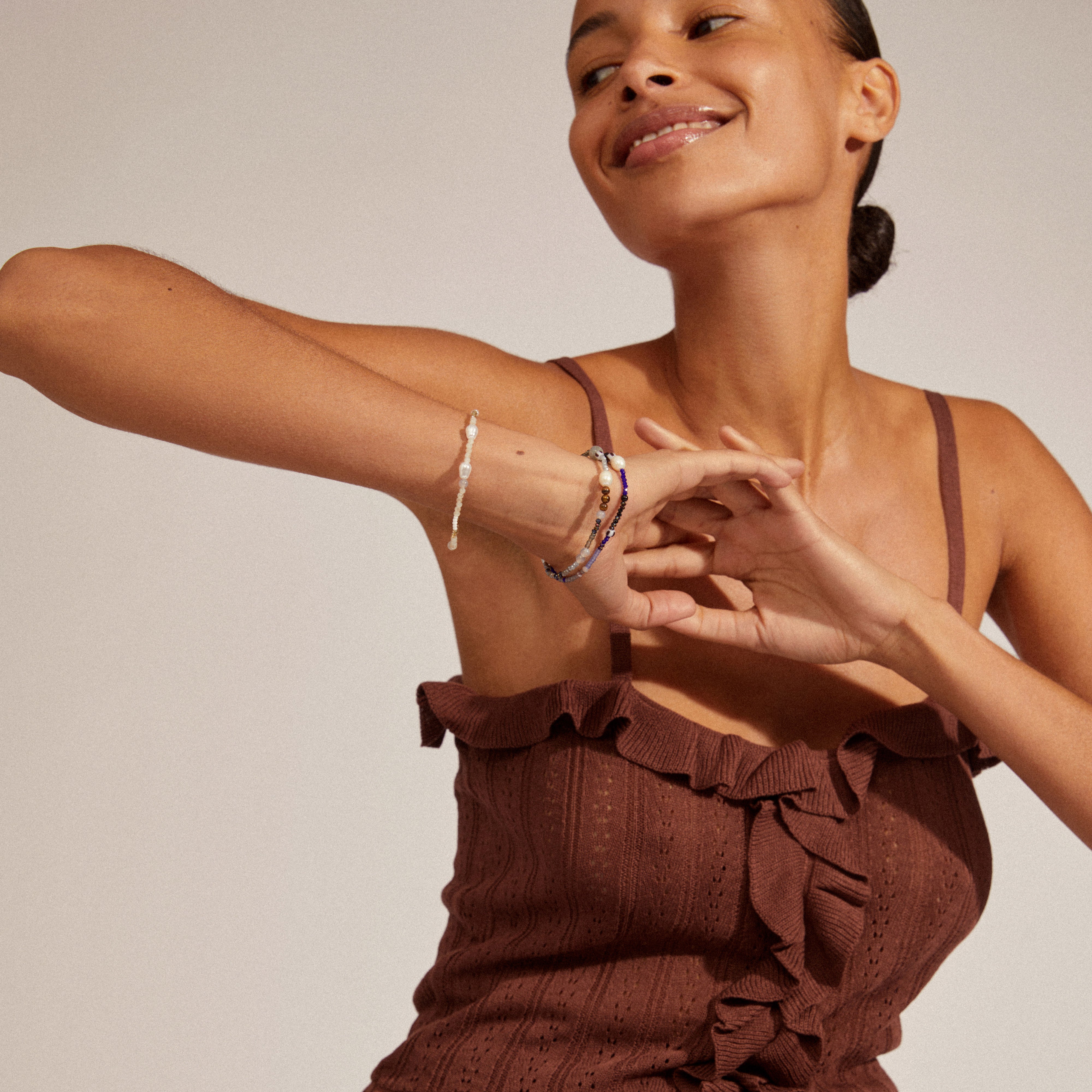 Woman wearing the INDIANA bracelet, showcasing its freshwater pearls, grey agate, and white-grey glass beads, highlighting its stylish, stacked look on her wrist.