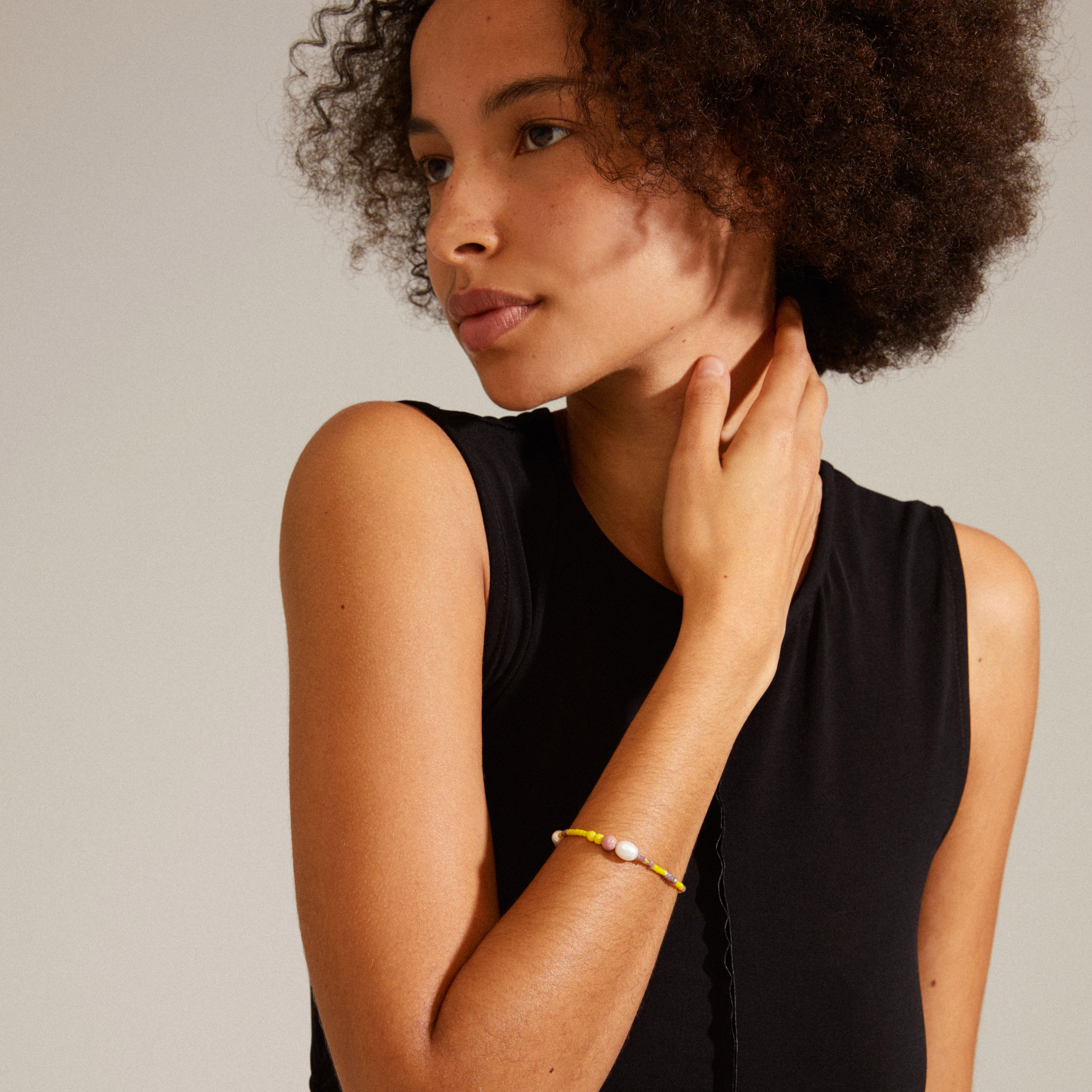 Close-up of the INDIANA bracelet yellow featuring freshwater pearls, pink opal, and faceted glass beads on a woman's wrist, showcasing its organic, trendy design.