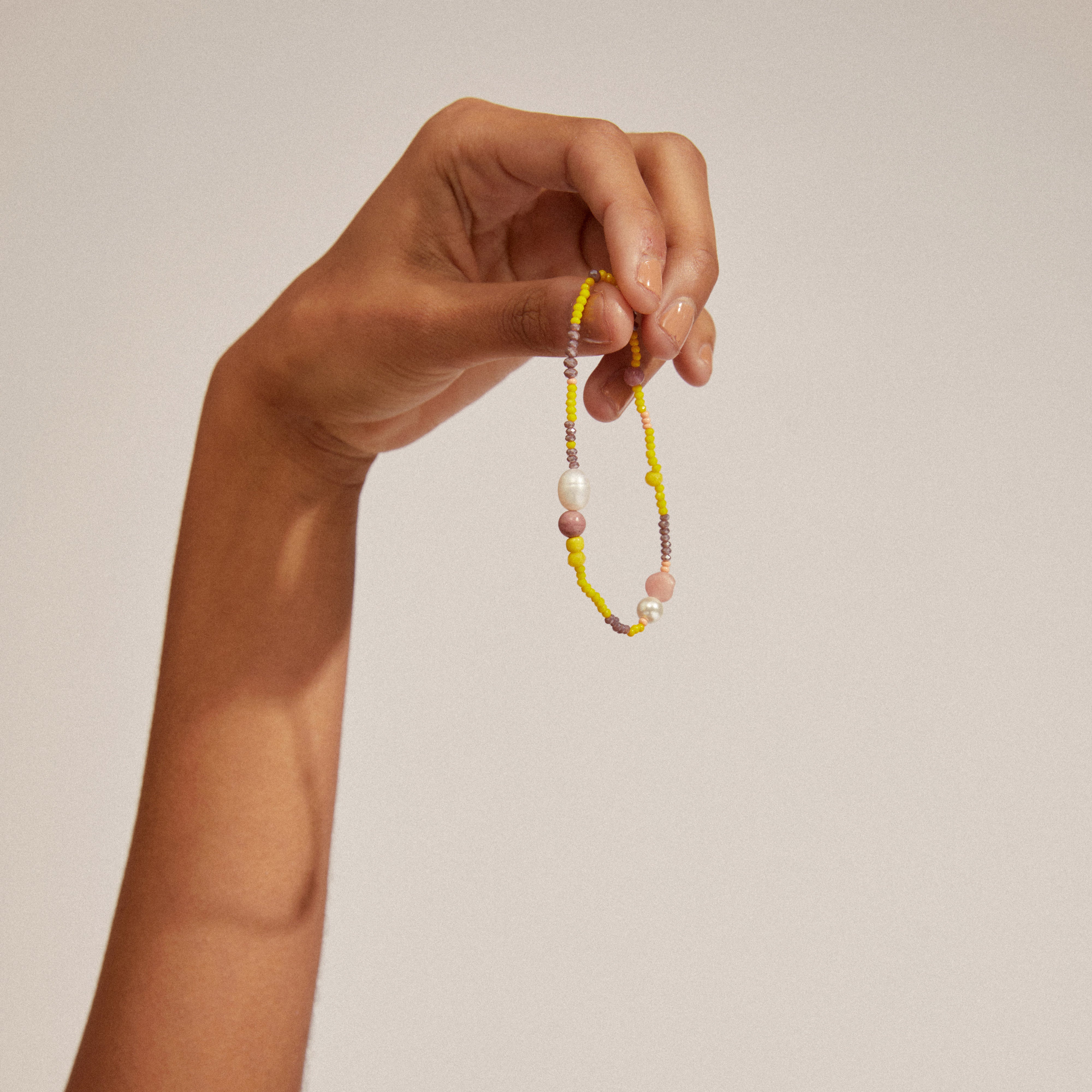 Hand holding the INDIANA bracelet, showcasing genuine freshwater pearls and pink opal stones, perfect for a stylish, stacked look with its organic design.