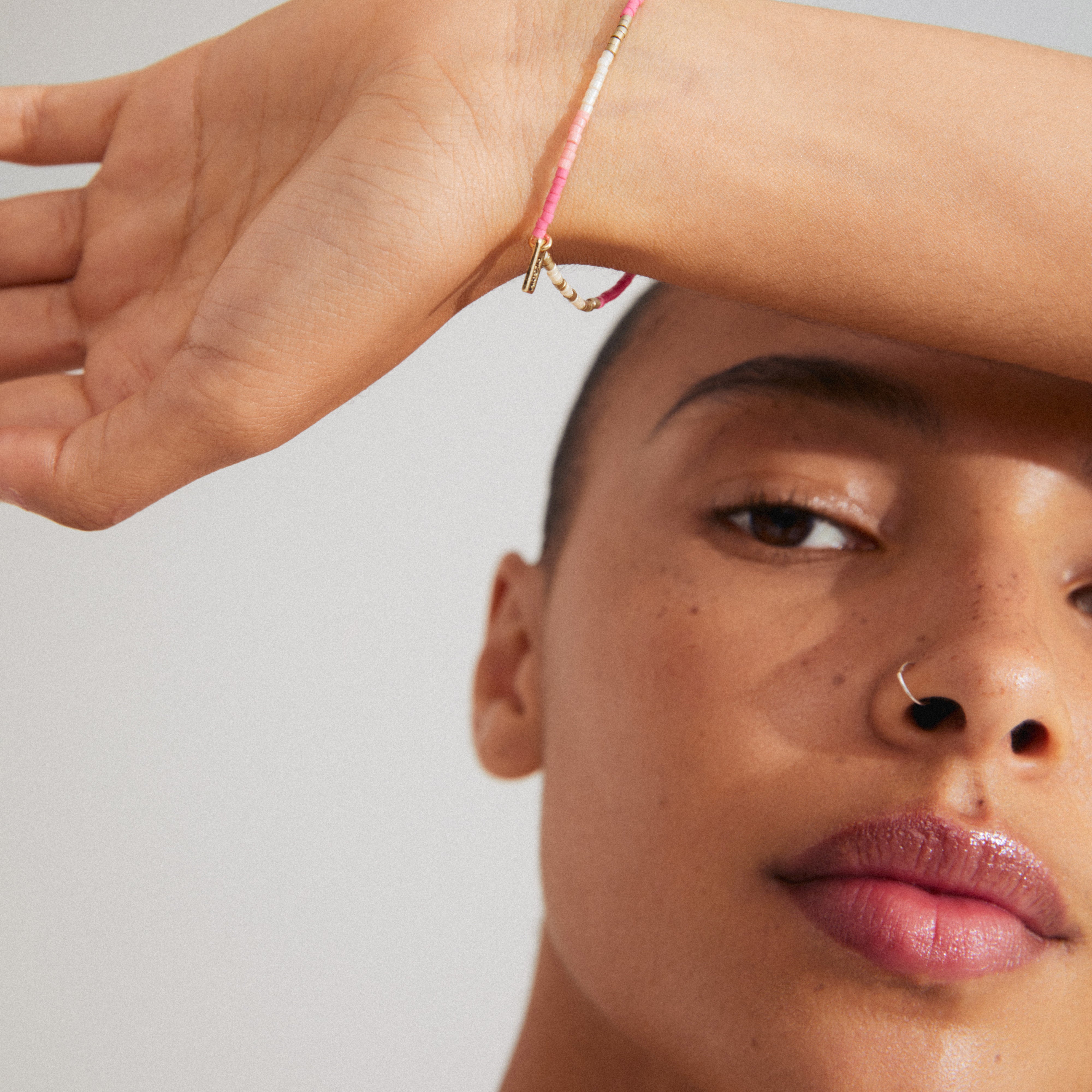 Close-up of a woman wearing the ALISON bracelet in pink, gold-plated, showcasing its intricate design with pink and grey glass beads.