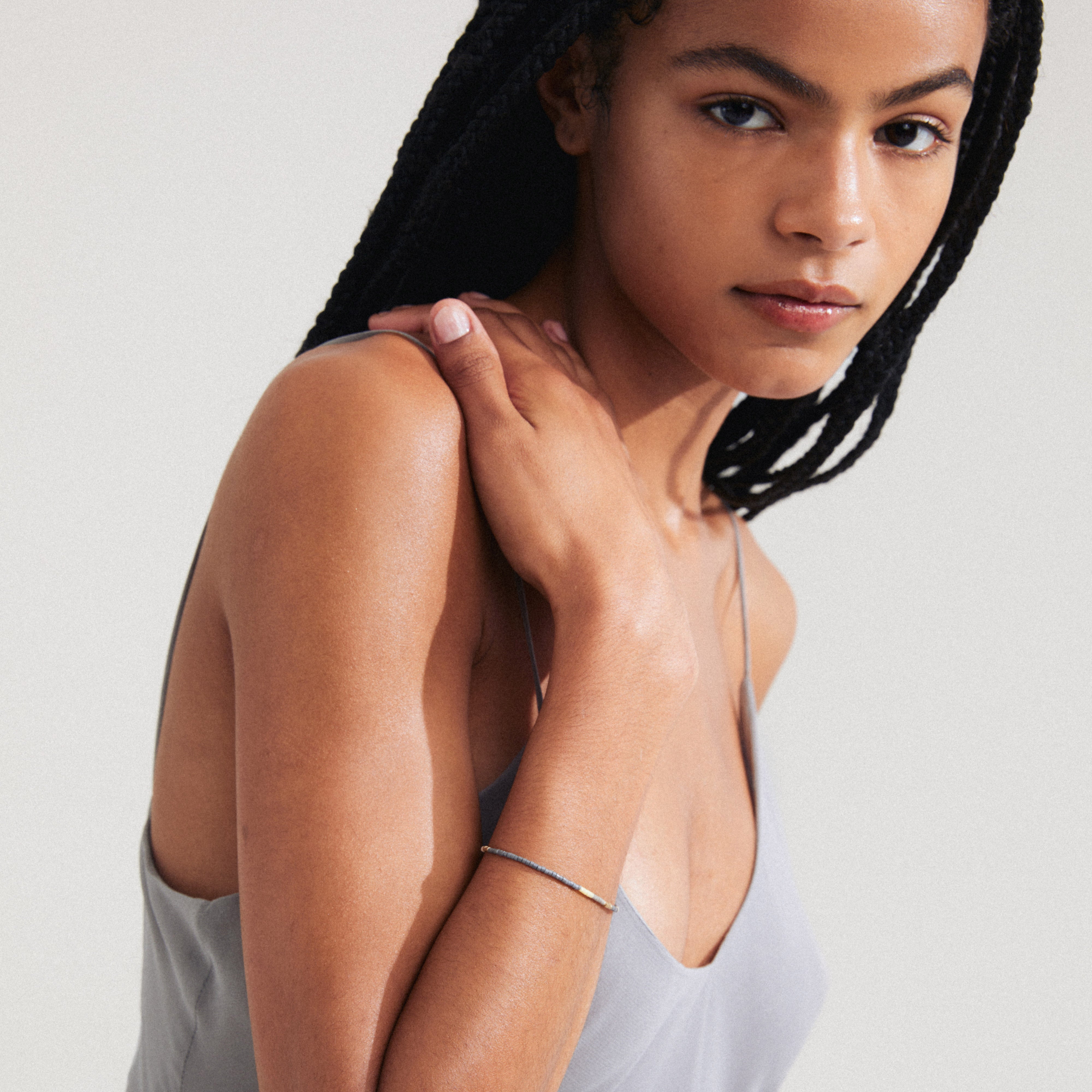 Woman with braided hair wearing the ALISON bracelet in silver-plated, featuring grey glass beads, perfect for creating a boho-chic, stackable accessory look.