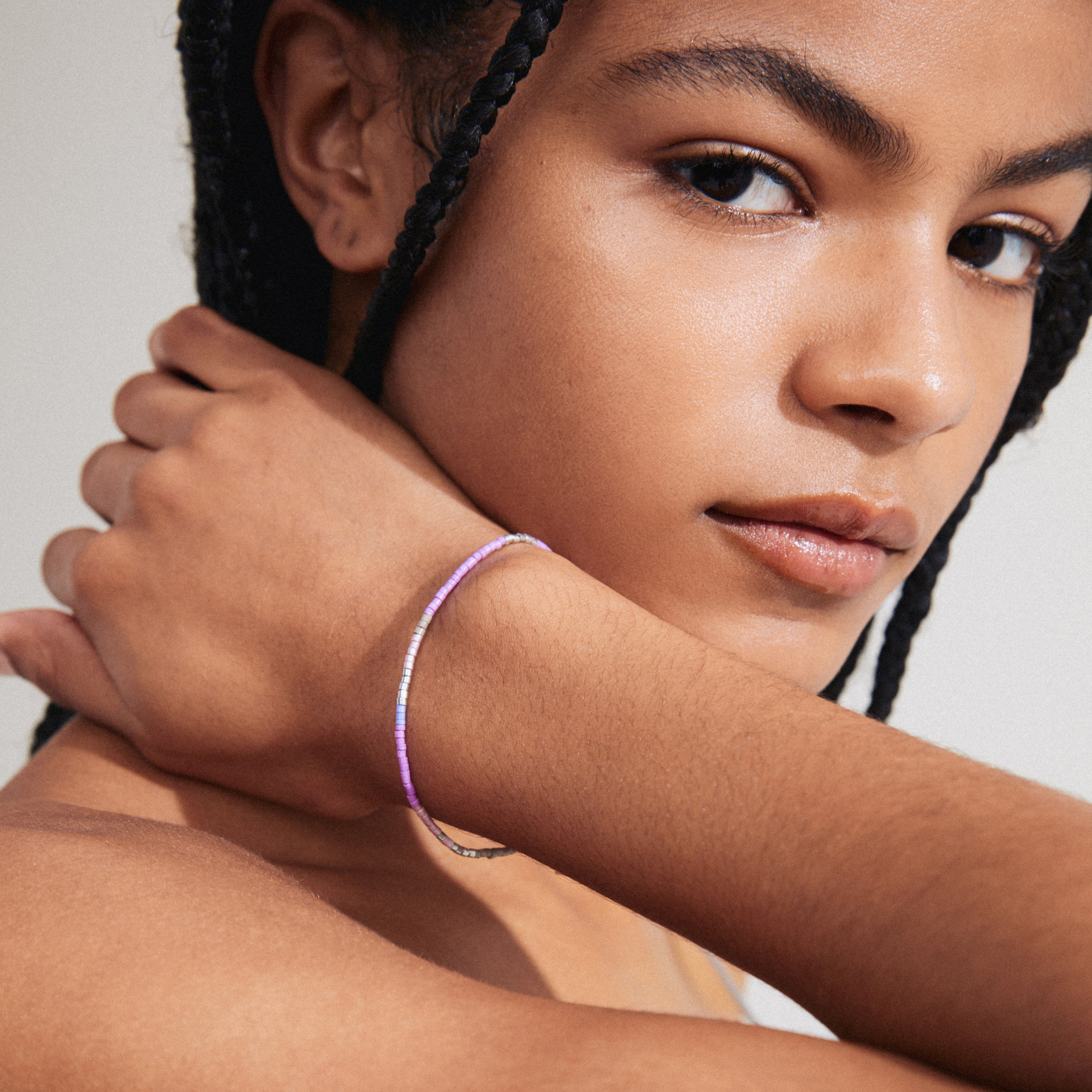 Woman with braids showcasing the ALISON bracelet in purple and silver-plated, featuring purple and grey glass beads on a durable lycra elastic band.