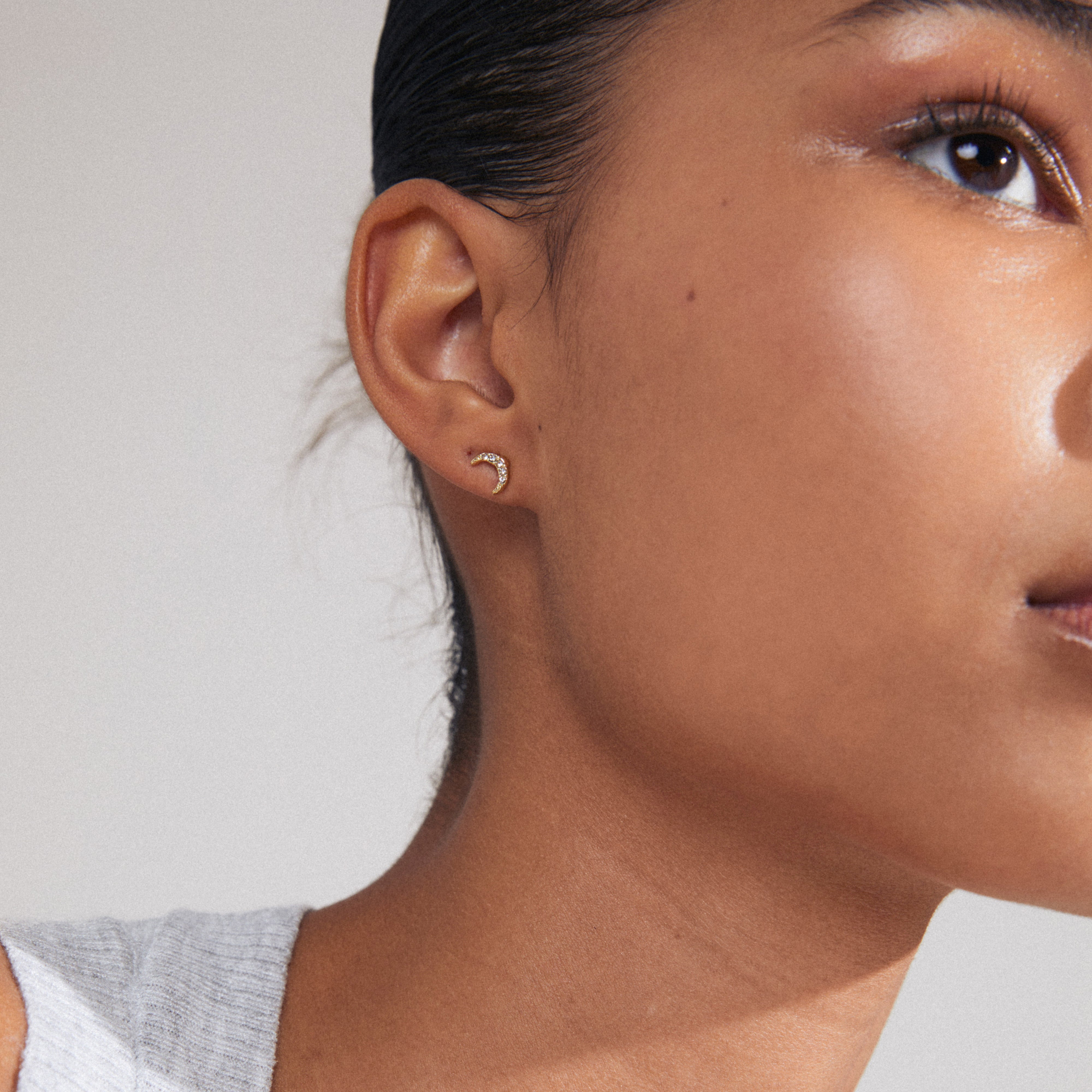 Close-up of a woman's ear adorned with the MELINA single gold-plated earring, featuring a crescent moon design with sparkling Preciosa crystals.