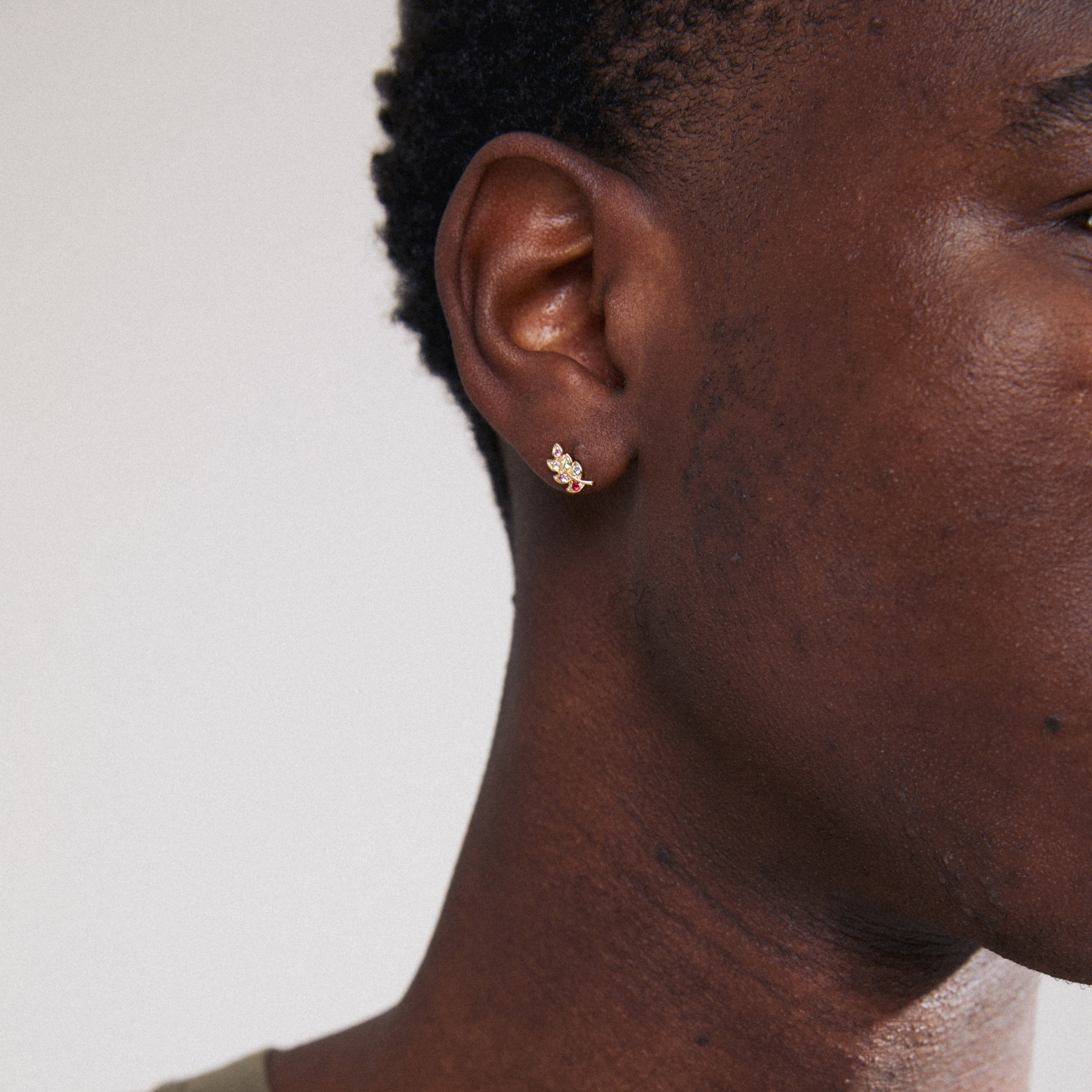 Close-up of a man's ear wearing the ARES single earring, a gold-plated leaf with colorful crystals by Pilgrim.