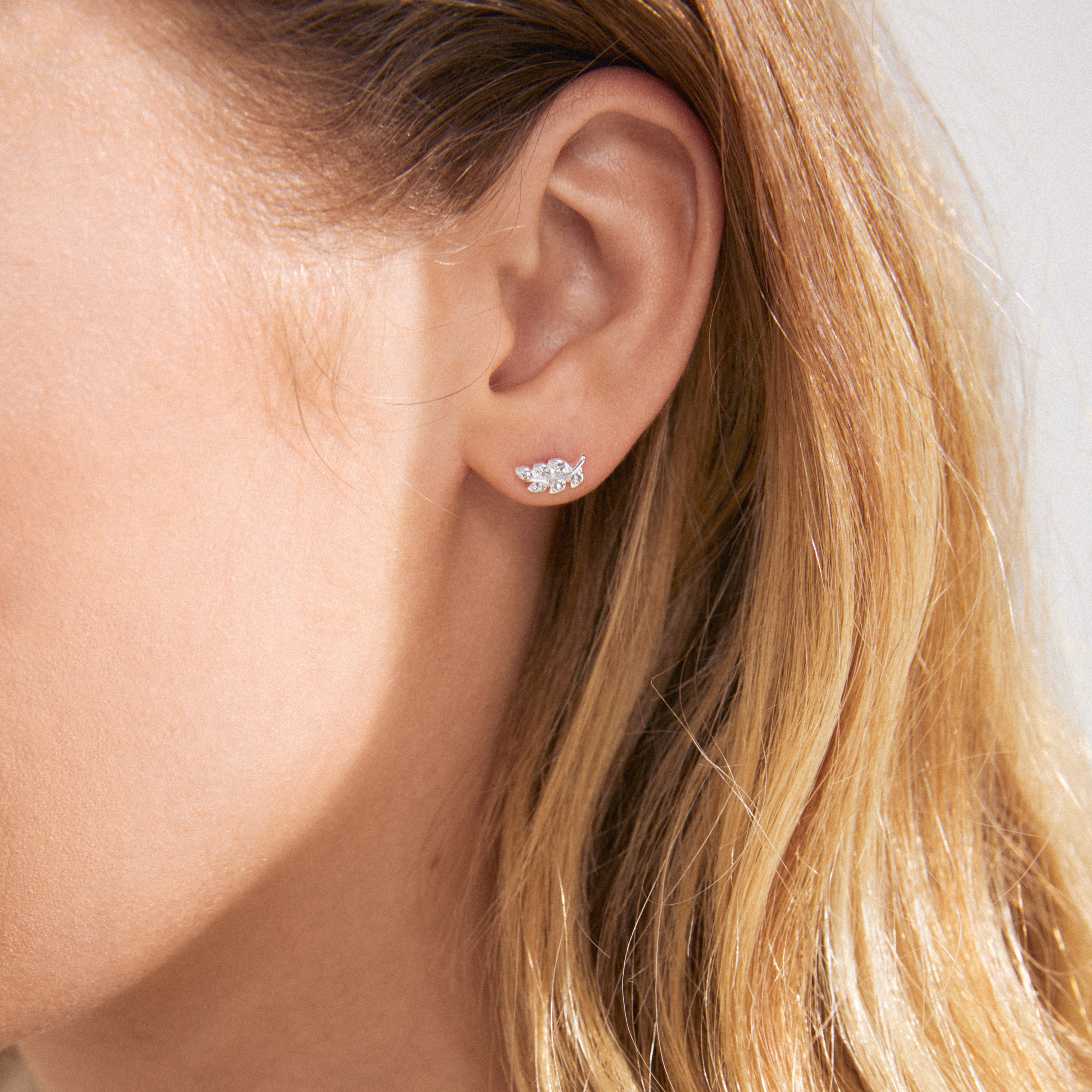 Close-up of a woman's ear adorned with the ARES single earring, a silver-plated leaf design with Preciosa crystals from Pilgrim's collection.
