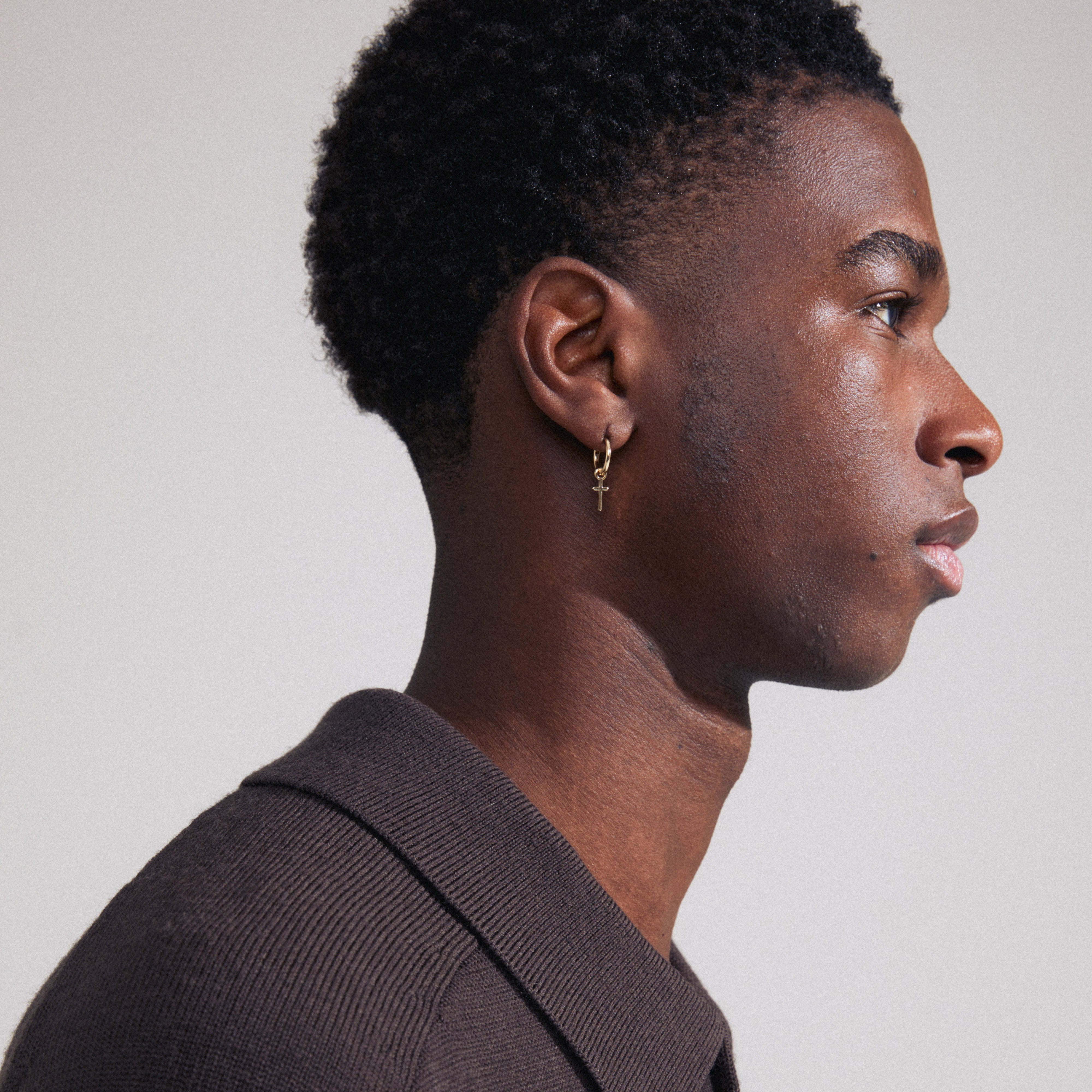XENAIA single earring gold-plated, featuring a small hoop with a cross pendant, visible in profile on a man's ear.
