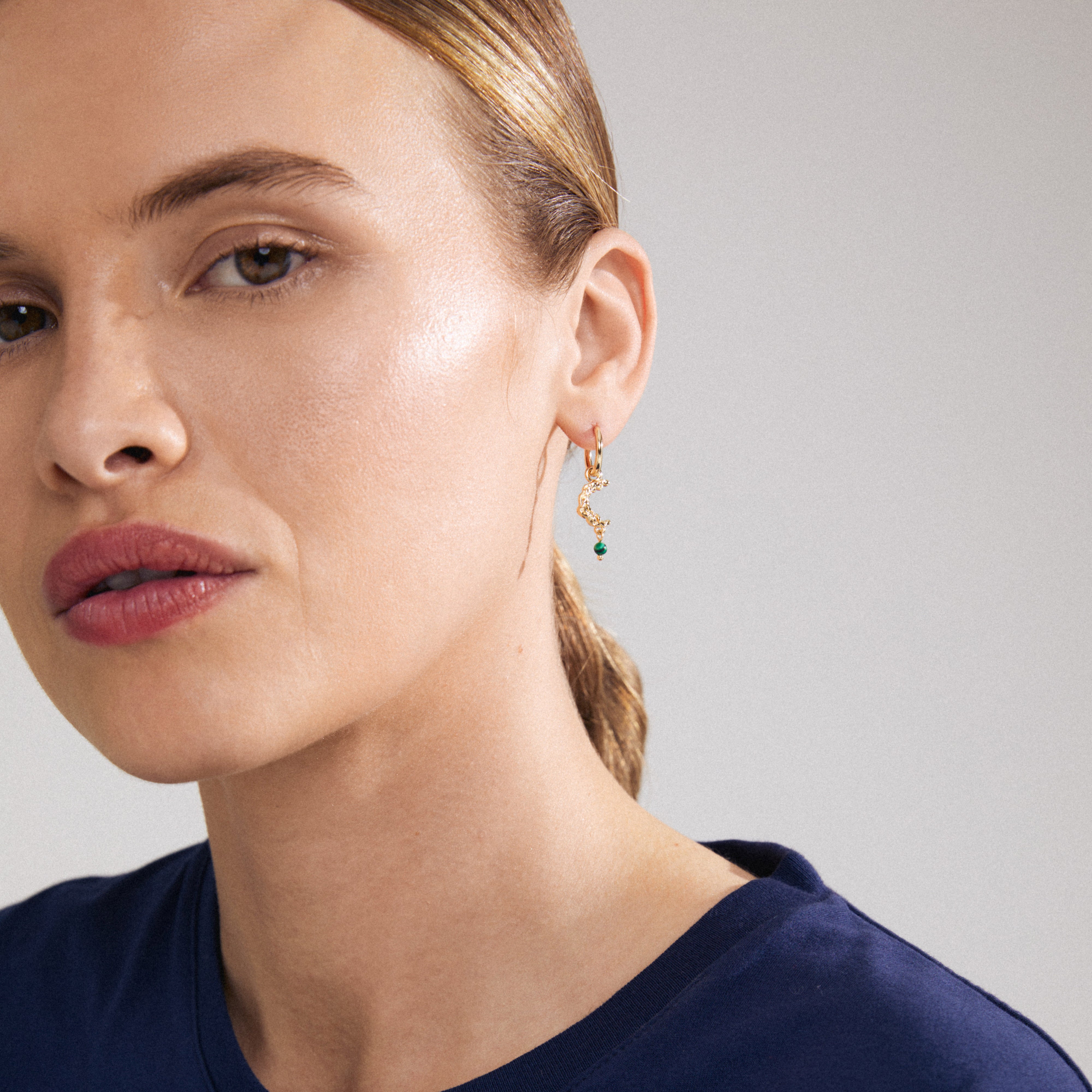 THERA single earring gold-plated with moon pendant and green stone, worn by a woman. Features a click clasp, crafted from recycled material.