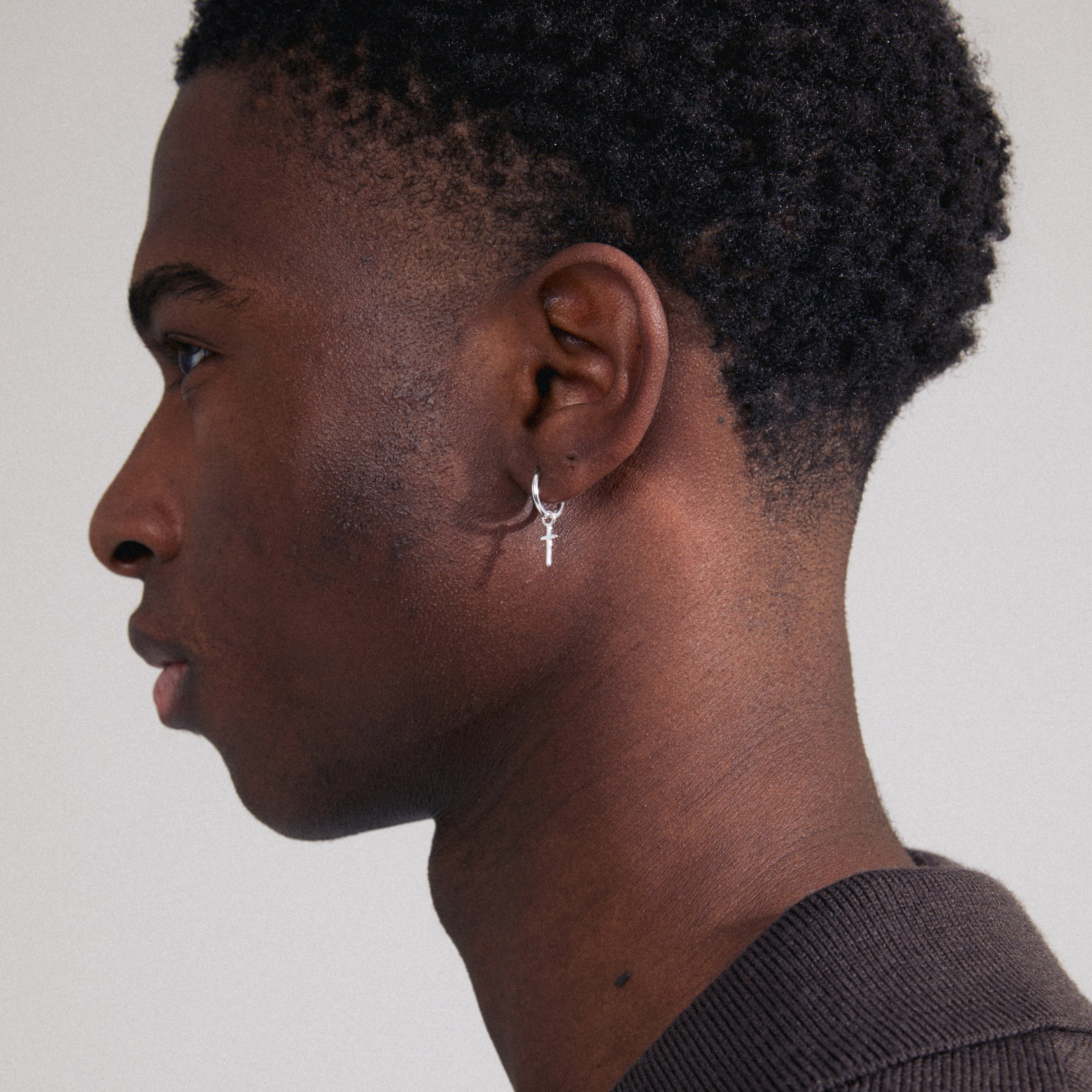 XENAIA single earring silver-plated, featuring a small hoop with a stylish cross pendant, showcased on a man's ear. Made from 99% recycled material.