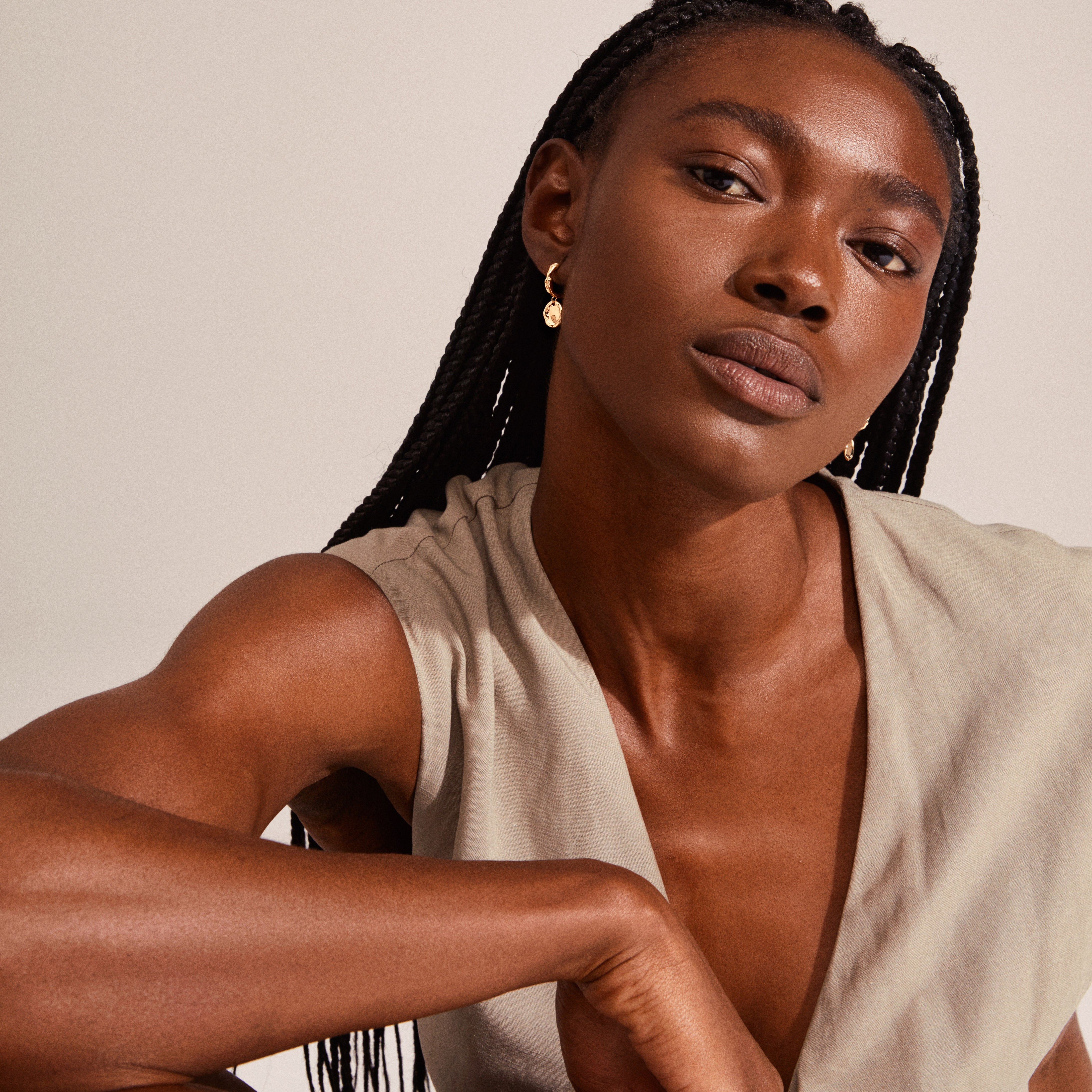 Woman with braids wearing Pilgrim's LEAF coin hoops gold-plated earrings, featuring decorative coin pendants and snap closures, showcasing a bohemian, sustainable design.