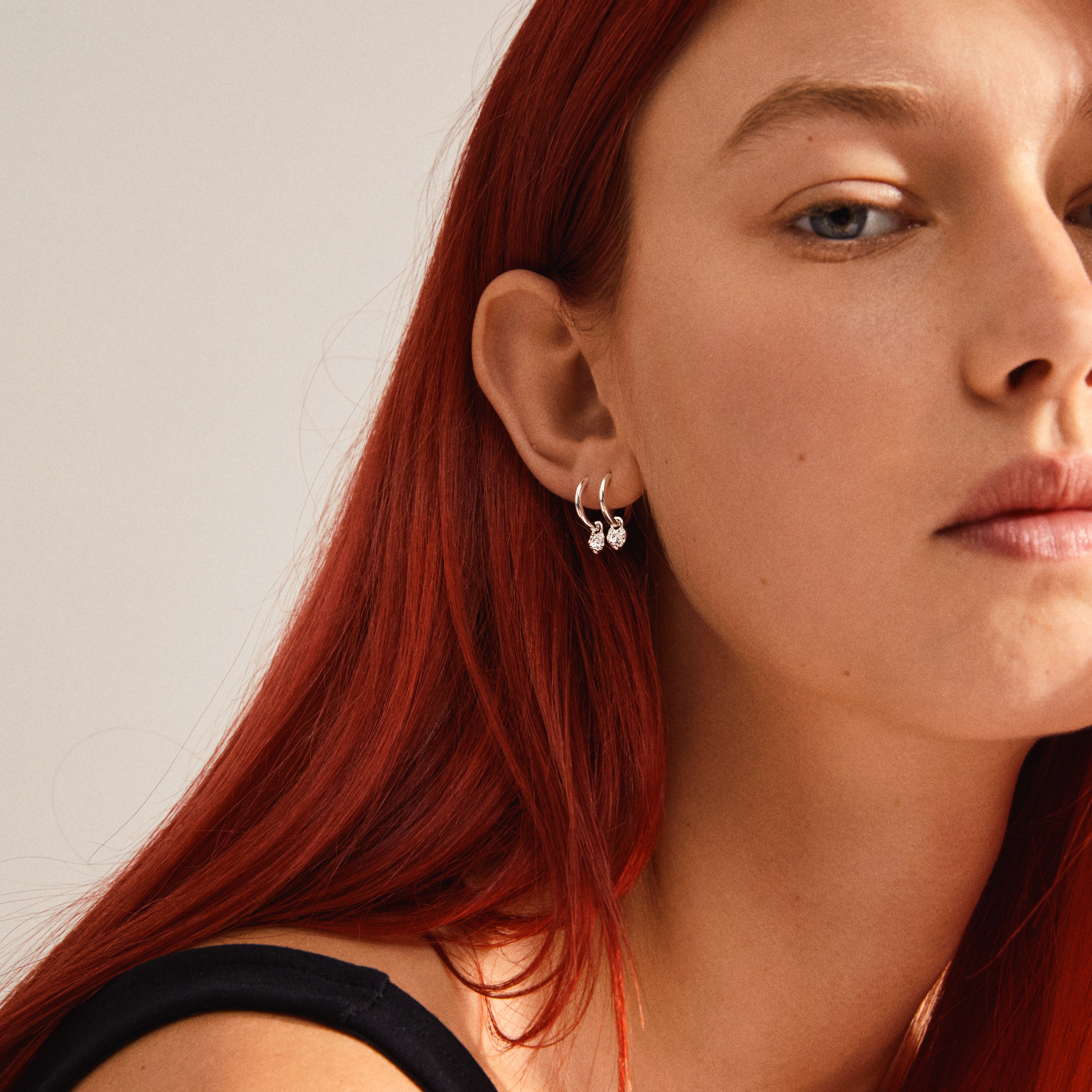 LEAF huggie hoops silver-plated adorn a woman's ear with heart pendants, showcasing Pilgrim's recycled jewelry collection's elegant and eco-conscious design.
