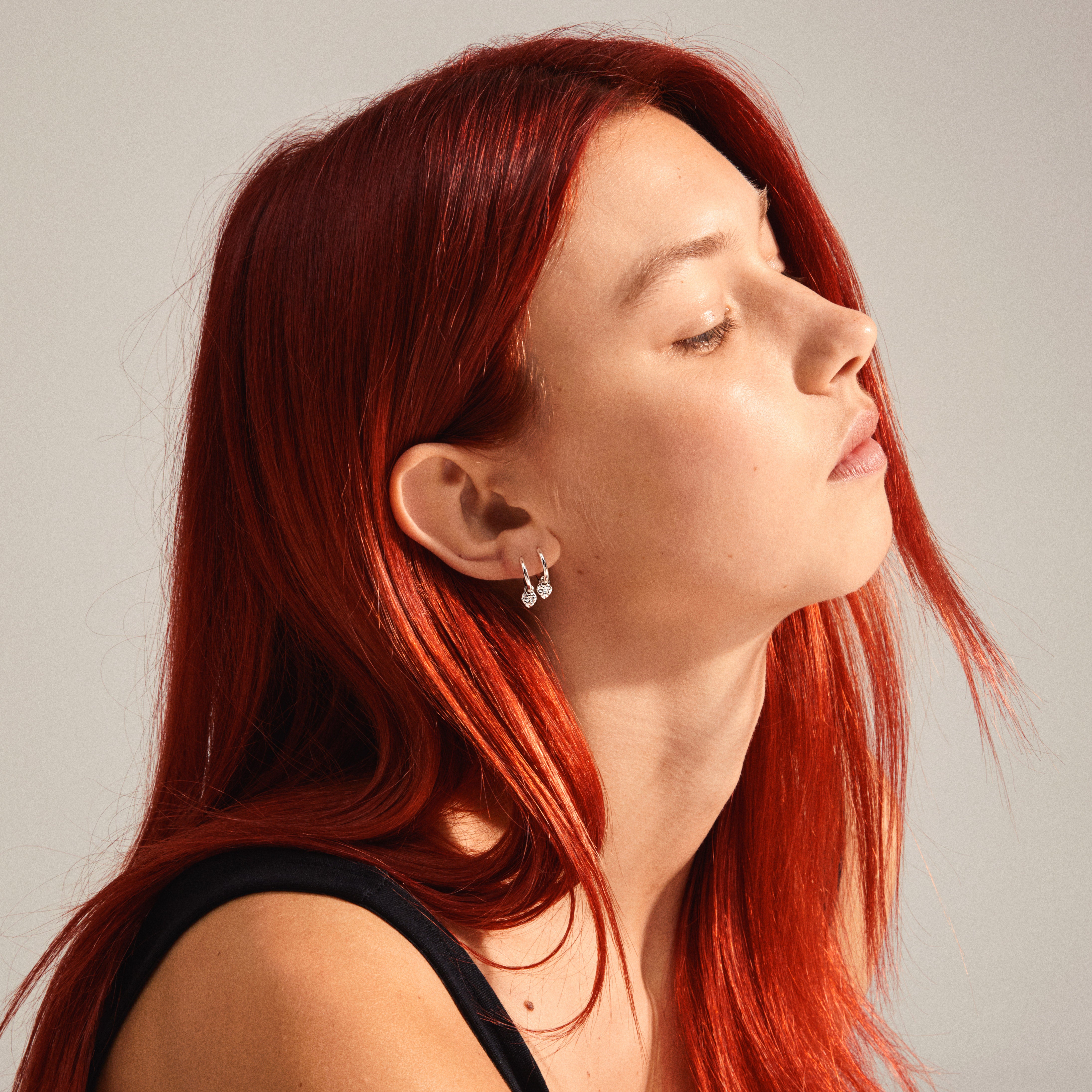 Close-up of a woman's ear wearing LEAF huggie hoops silver-plated with heart pendants, showcasing Pilgrim's recycled jewelry collection.