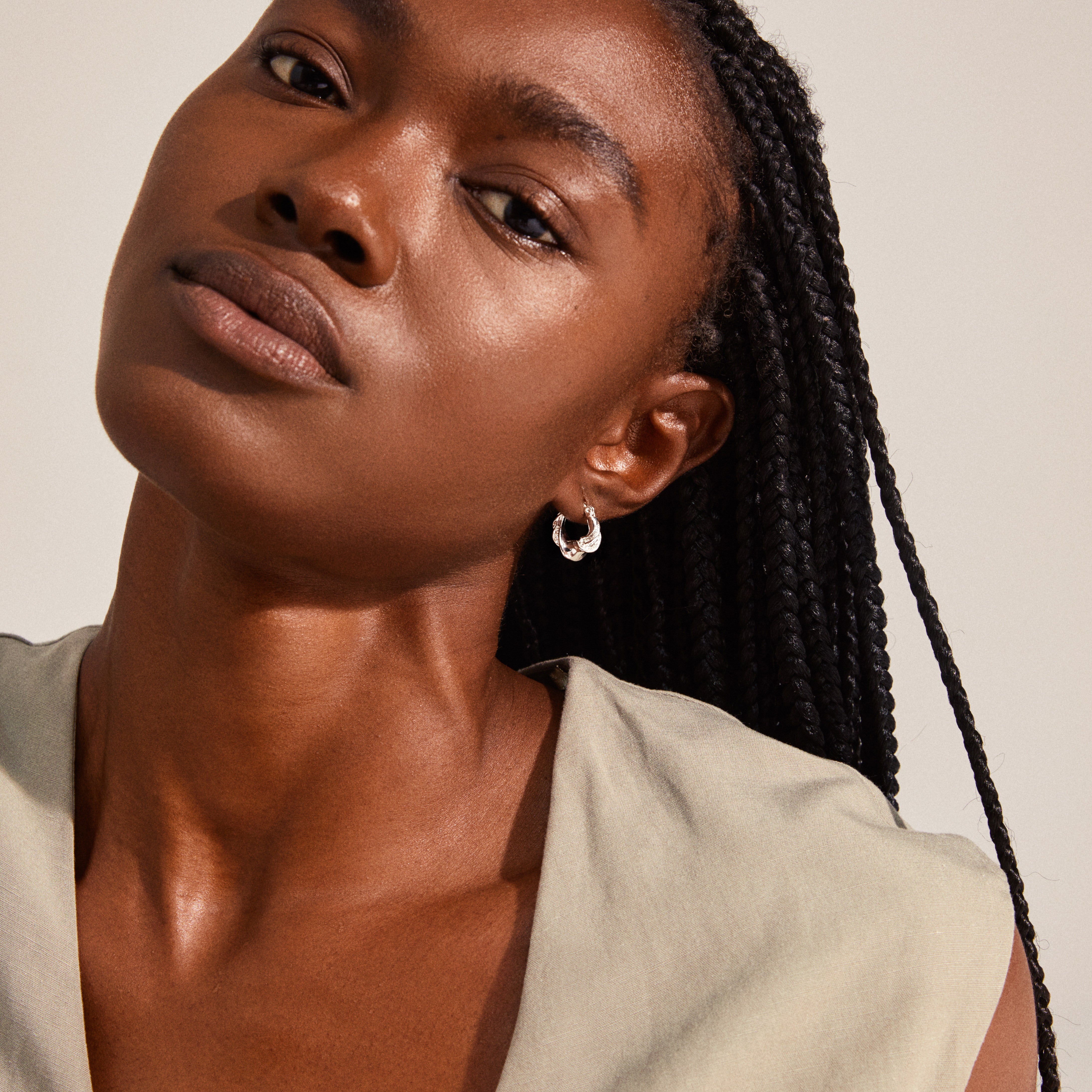 Silver-plated LEAF twirl hoops on a woman with braided hair, showcasing the chunky twisted design and sustainable craftsmanship from Pilgrim's recycled collection.
